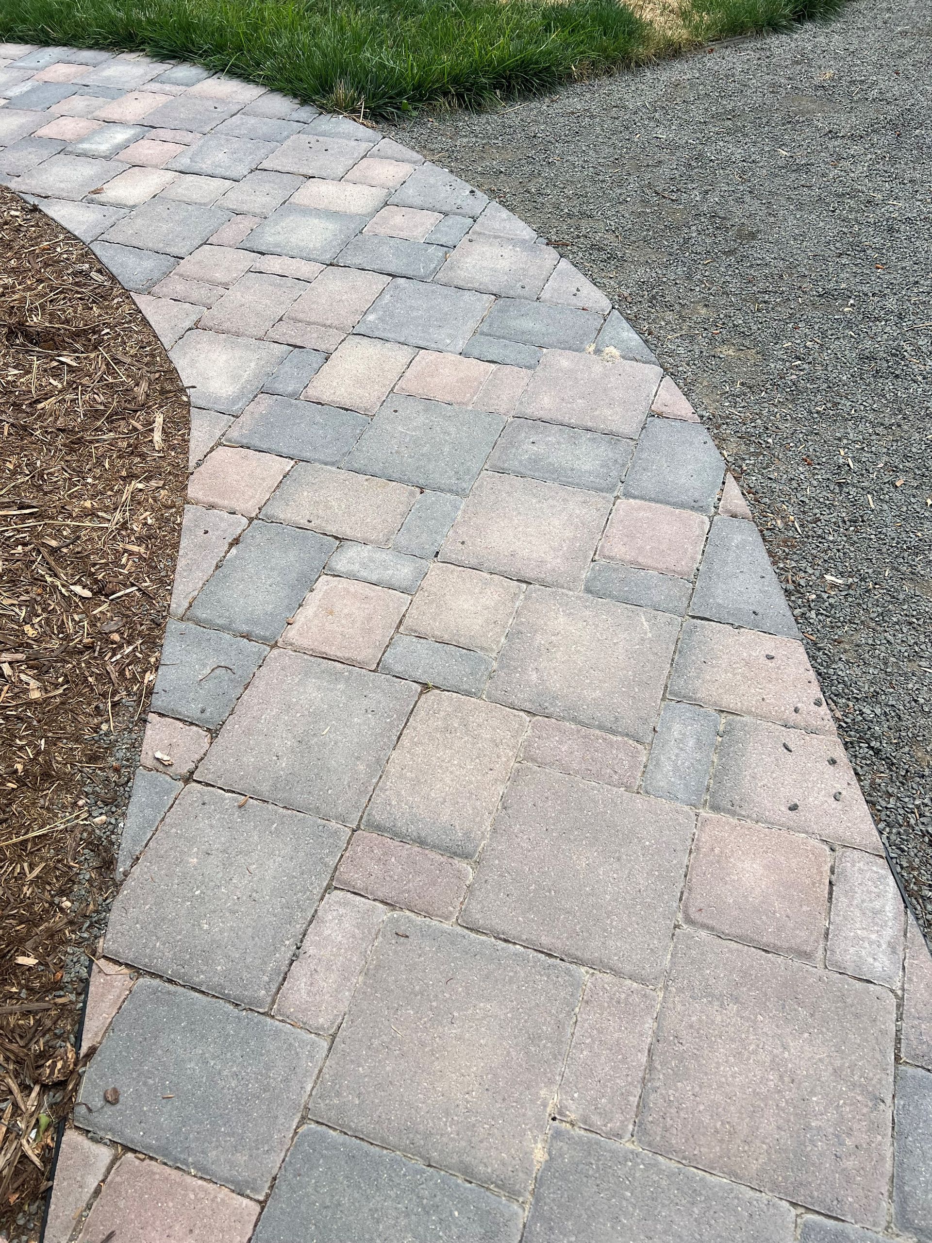 Curved brick pathway alongside gravel and mulch bed, with green grass in the background.