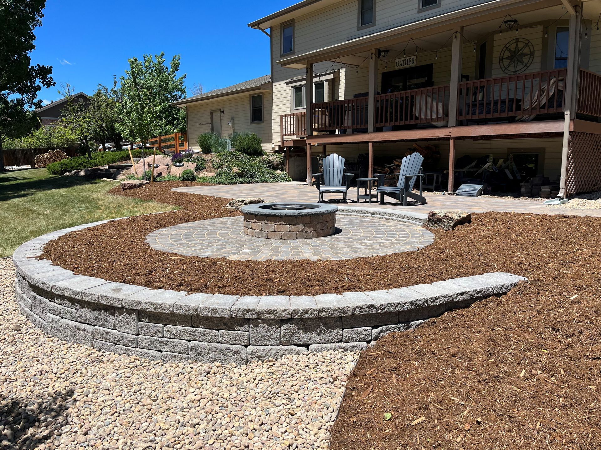 Backyard patio with fire pit, raised bed, seating, and house with deck.