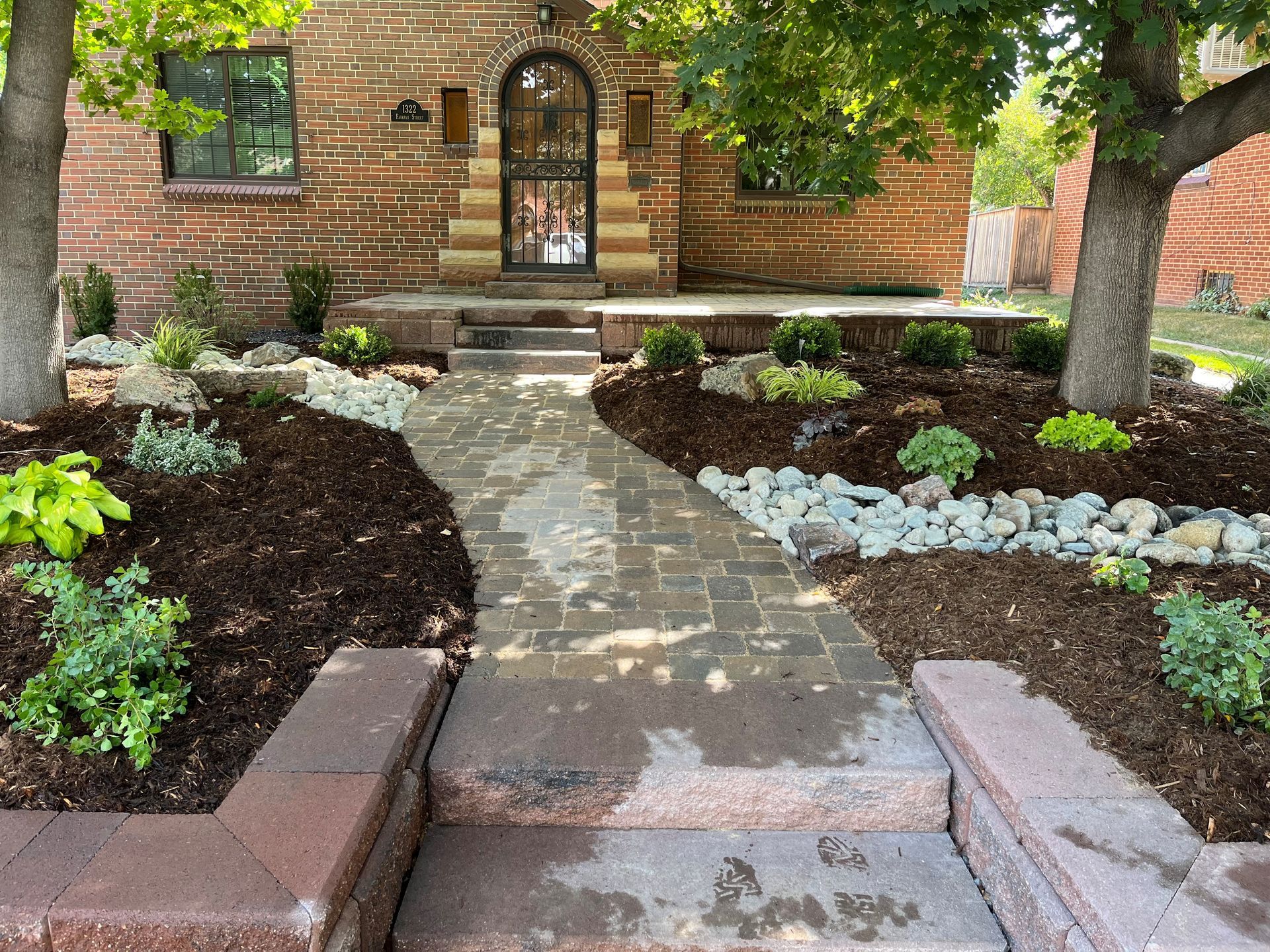 Brick home with a brick path leading to the front door. Landscaped front yard with plants, rocks, and mulch.