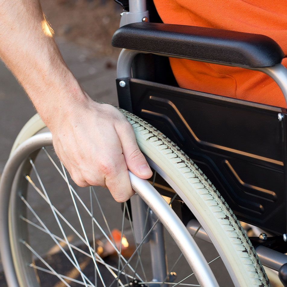 Hand pushing a wheelchair wheel with white tire and silver spokes beside an orange seat