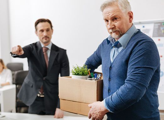 Businessman holding a box while another man points in an office, suggesting a job termination or exit.