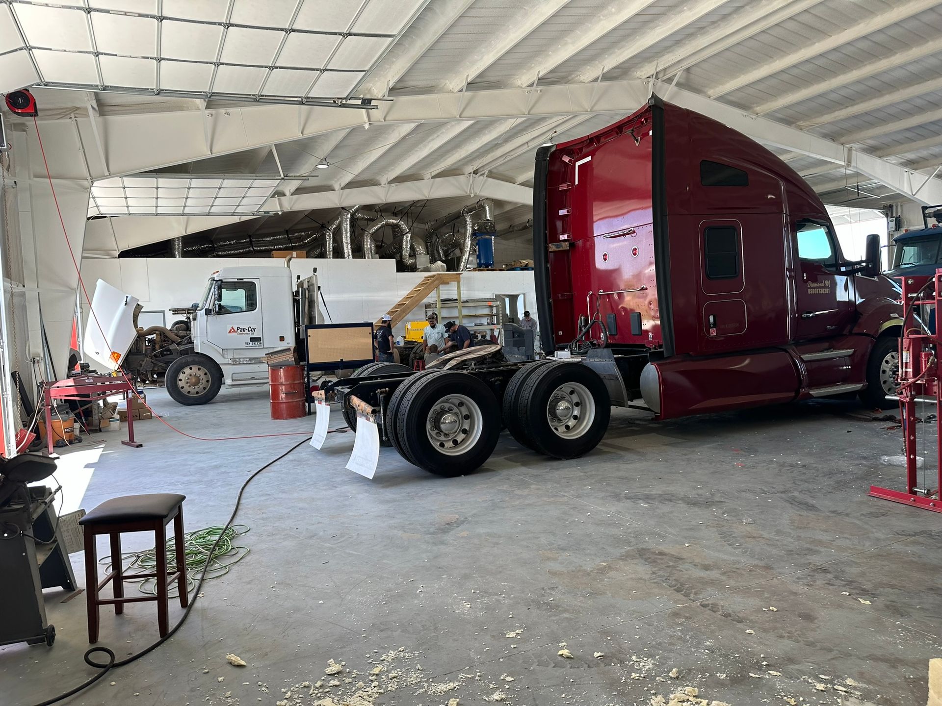 A red semi truck is being repaired in a garage.