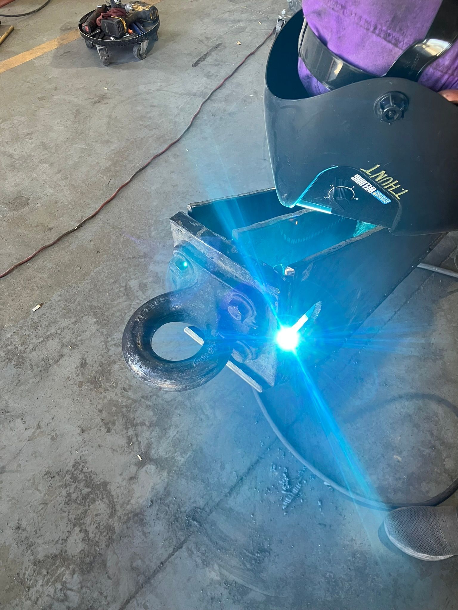 A person wearing a welding helmet is welding a piece of metal.