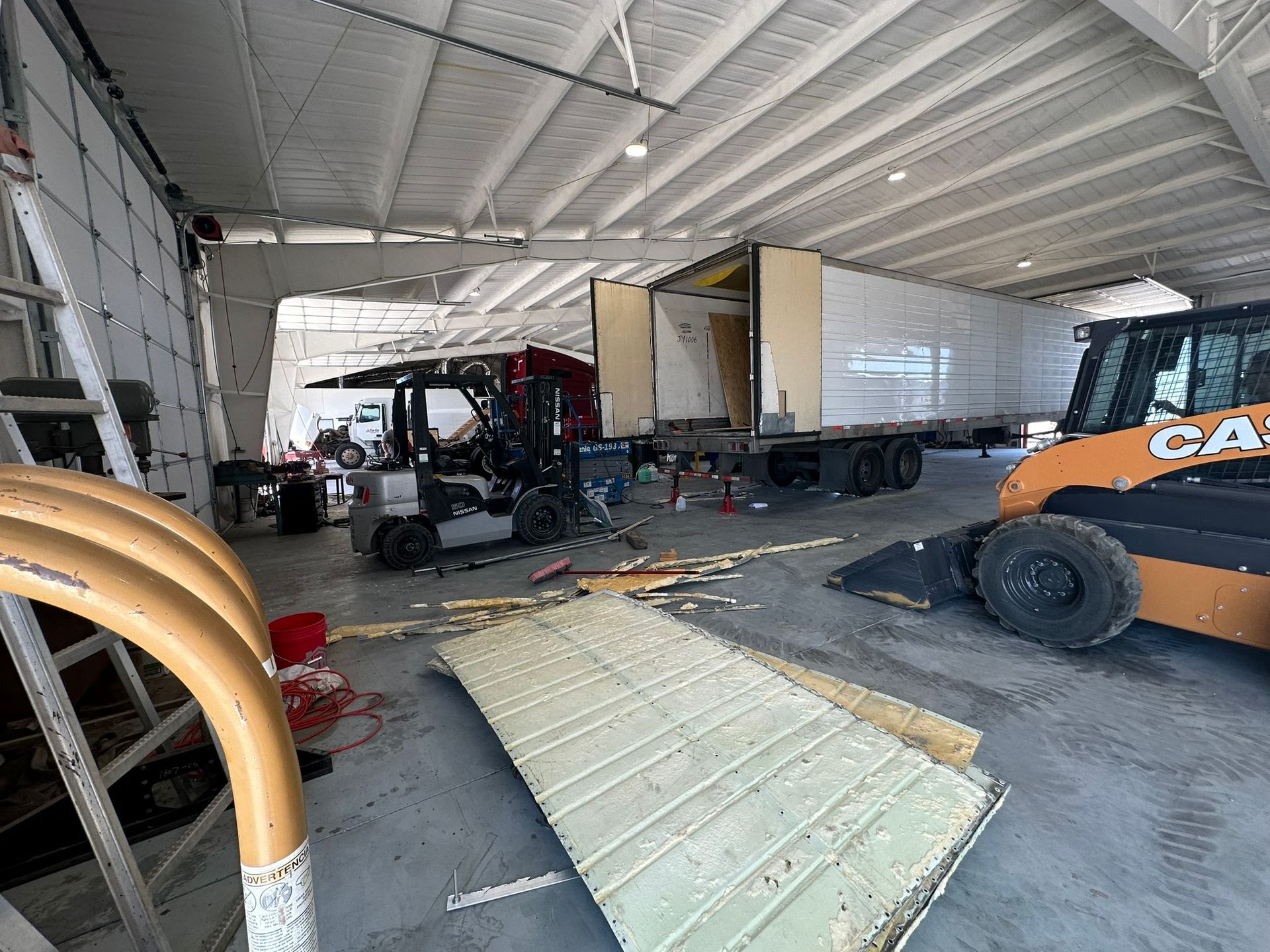 A forklift is parked in a garage next to a truck.
