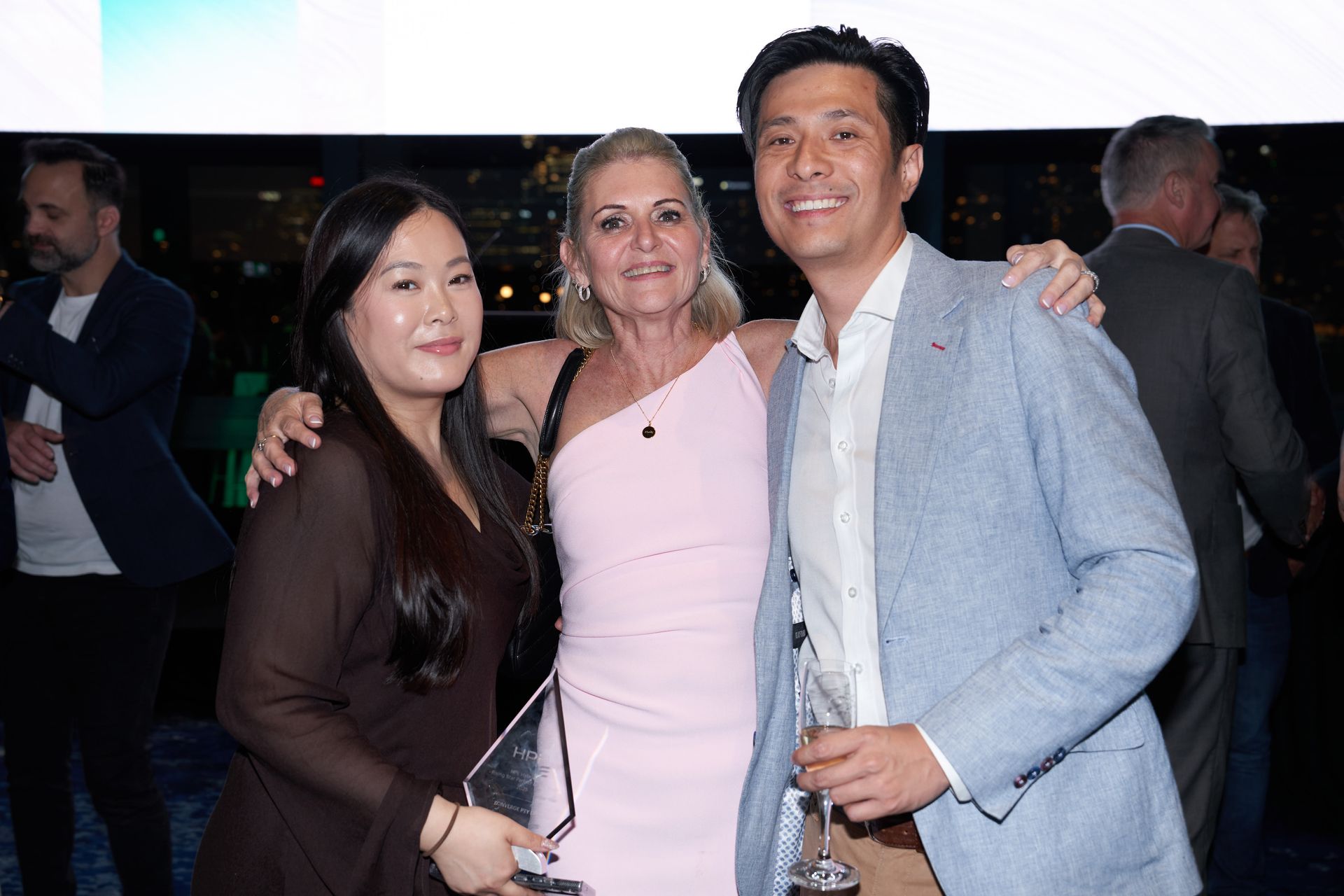 Three people smiling for a photo, one holding an award, at an event.