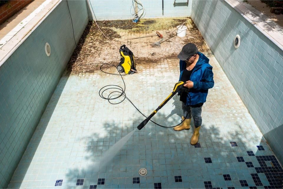 Person power washing a dirty, empty swimming pool.