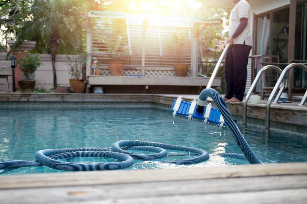 Person cleaning a swimming pool with a brush and hose.