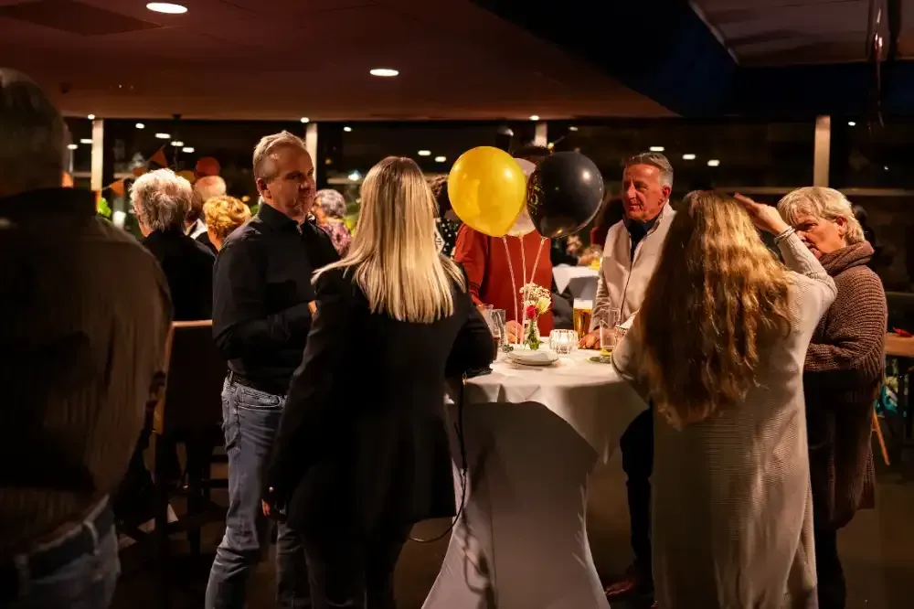 een groep mensen staat op een feestje rond een tafel met ballonnen.