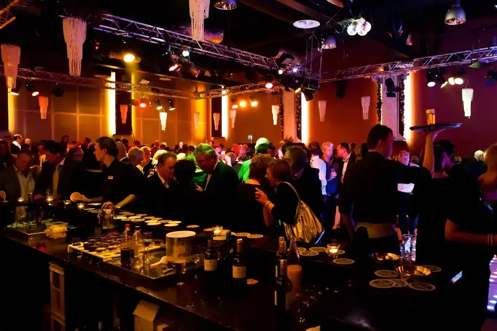 een menigte mensen verzamelt zich rond een bar in een donkere kamer.