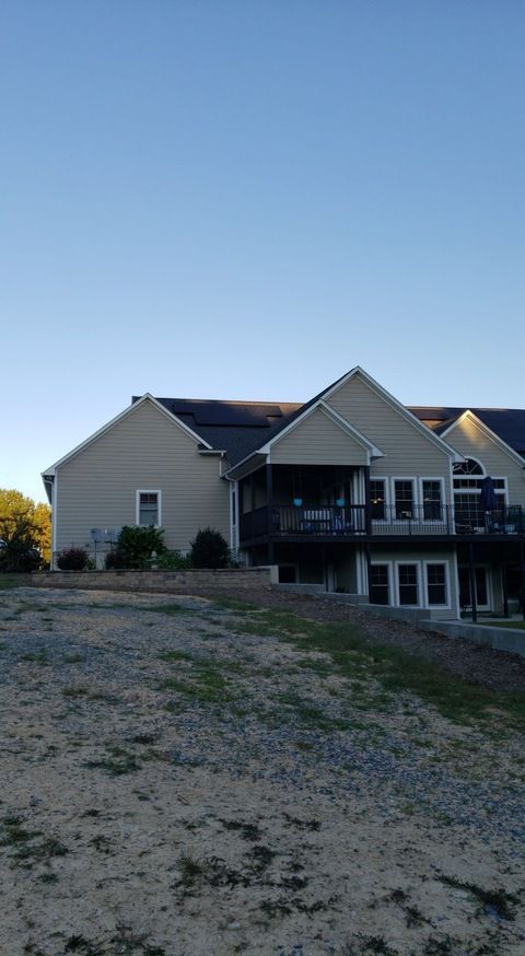A large house with a large deck is sitting on top of a dirt field.