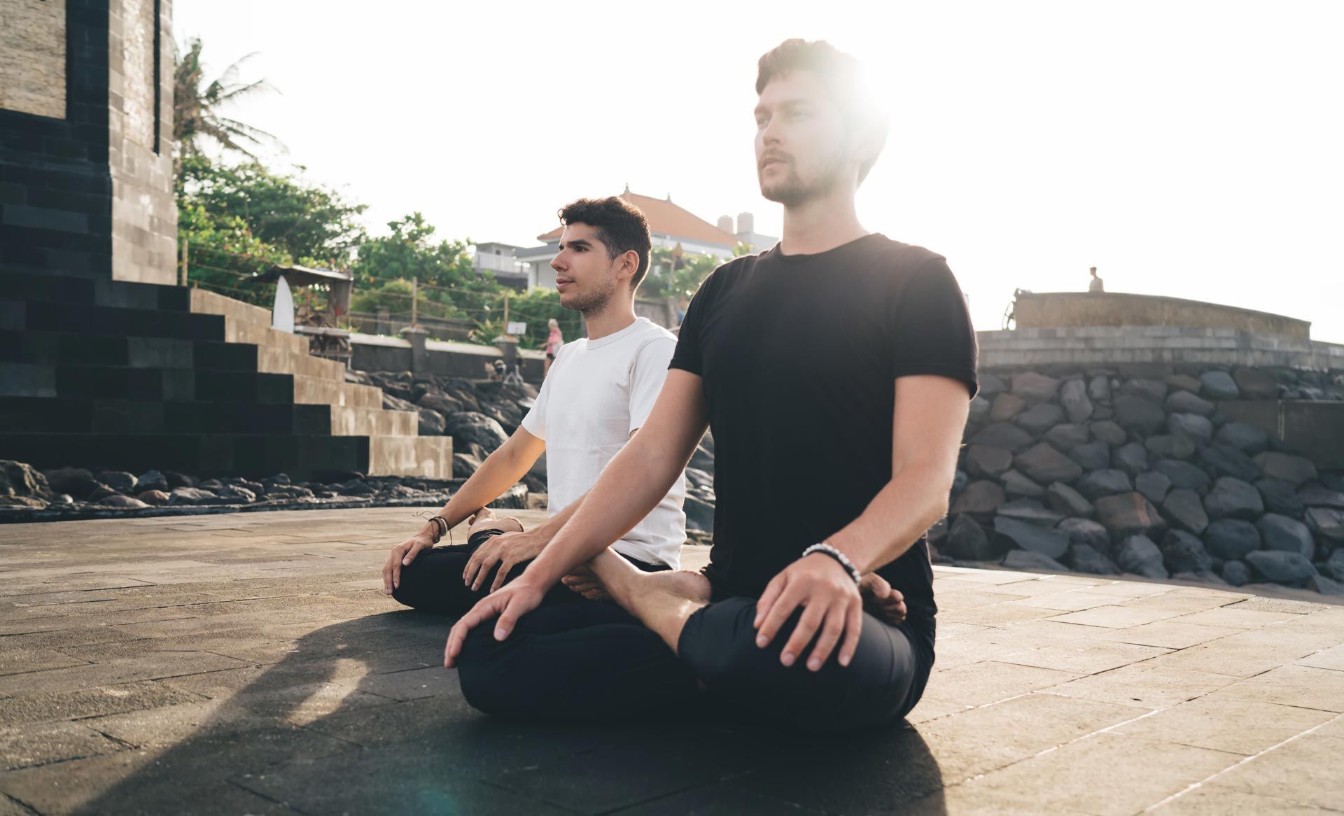 Two people sit cross-legged on a rooftop at sunset, meditating in black and white clothing.