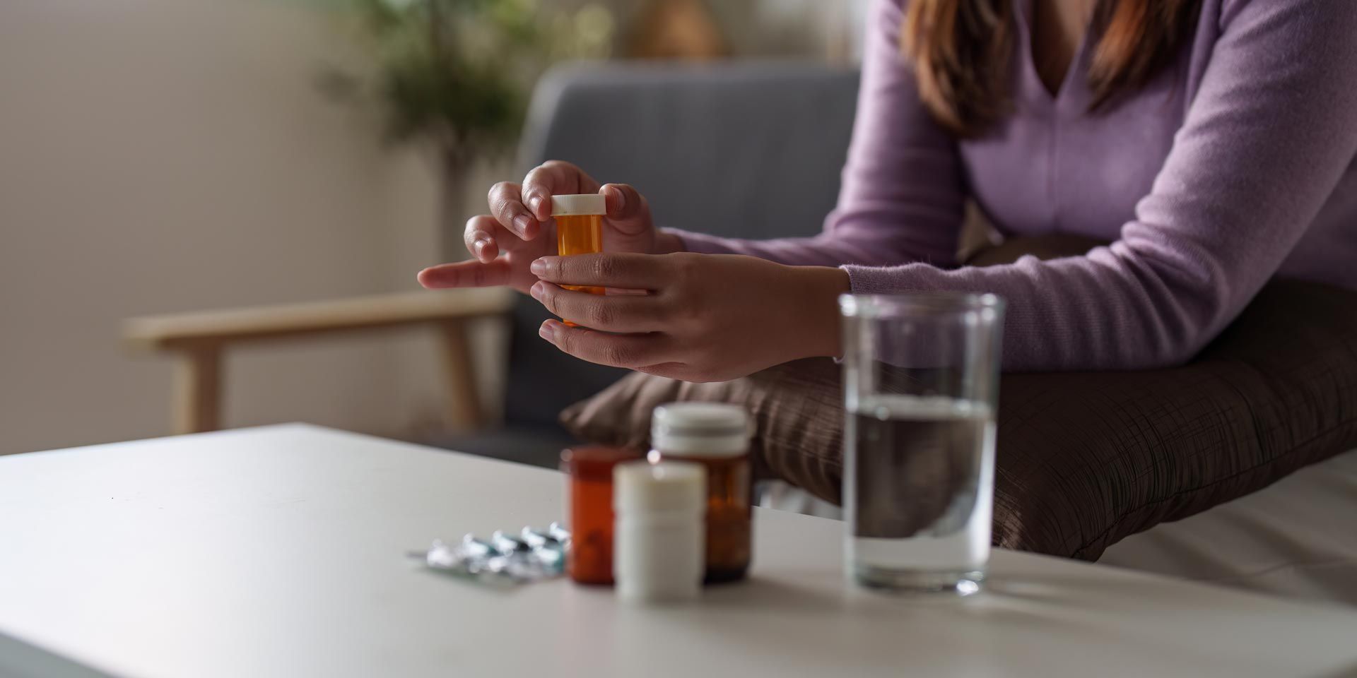 Person holding medicine bottles beside a glass of water on a table