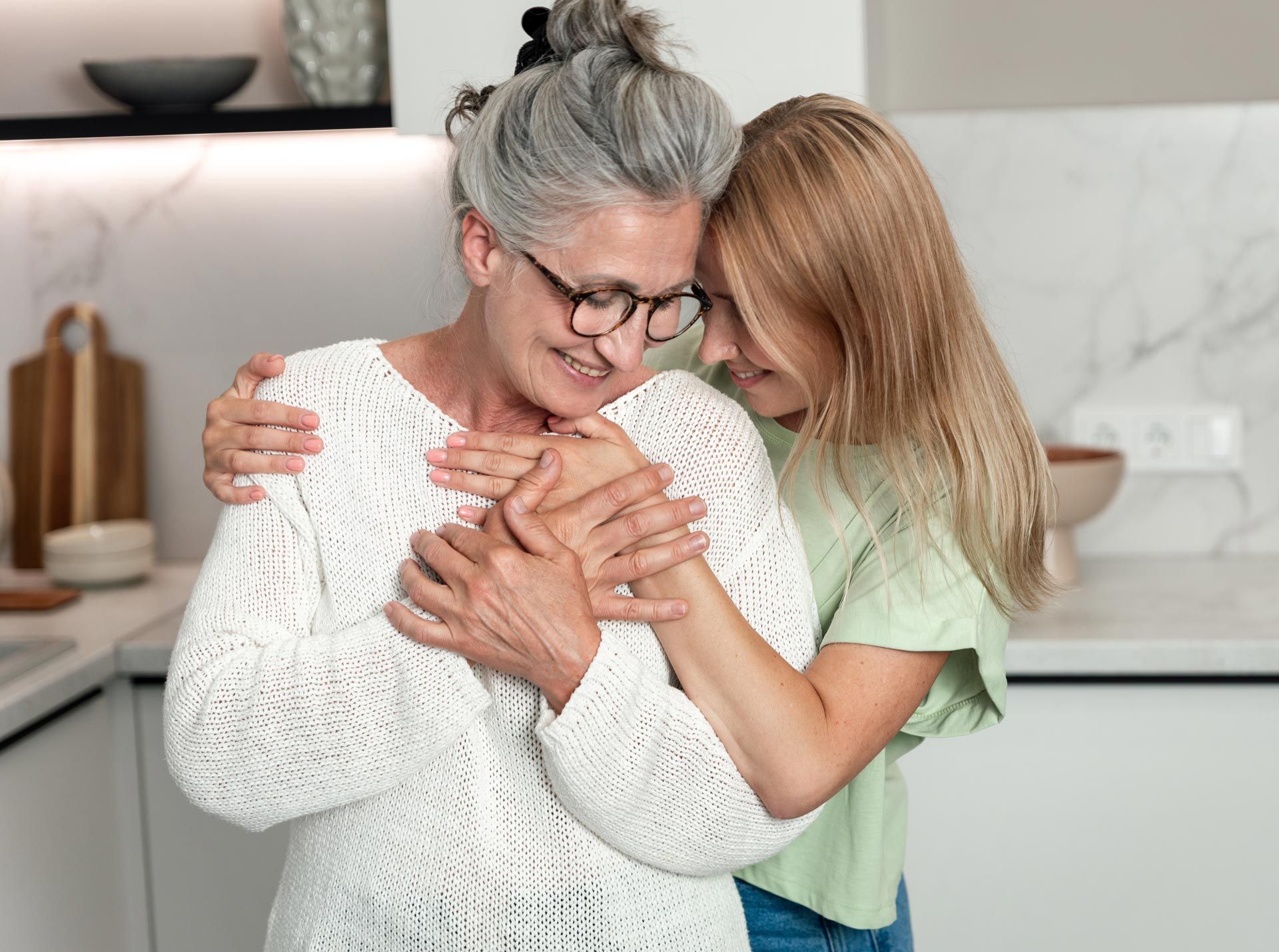 Two people embracing in a bright kitchen, smiling with eyes closed