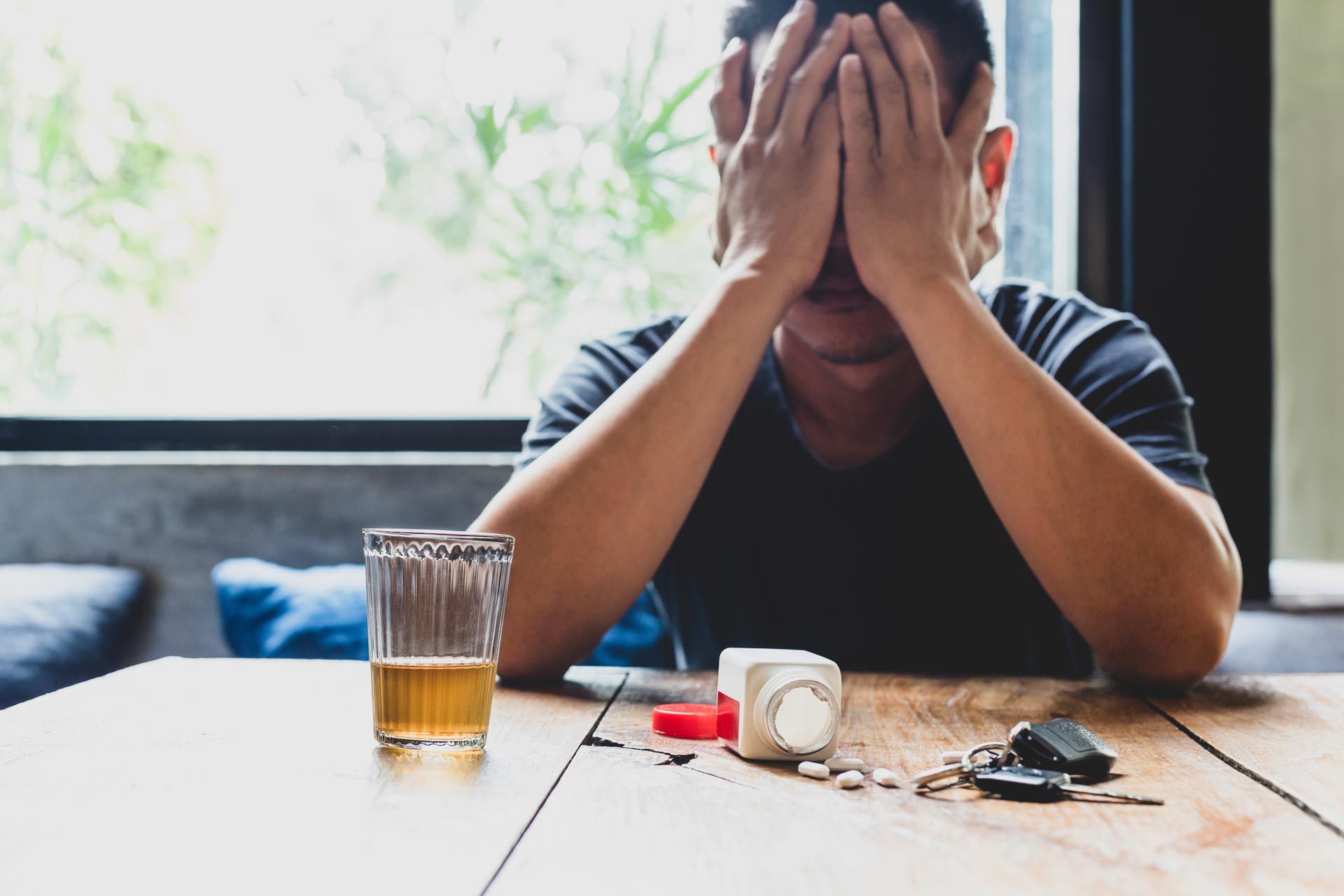 Person sitting at a table with head in hands beside a drink and car keys, looking stressed