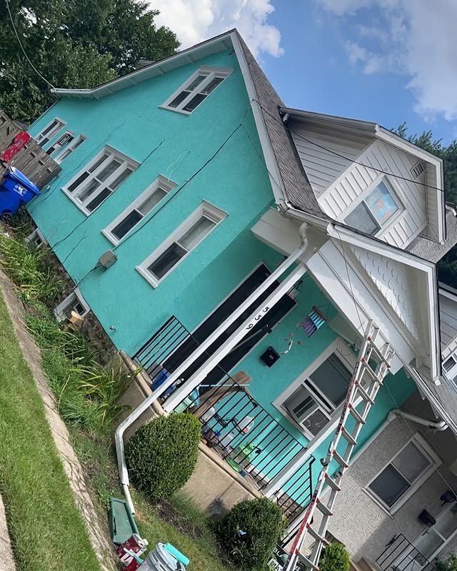 Teal-colored multi-story house with white trim; ladder leans against the front.