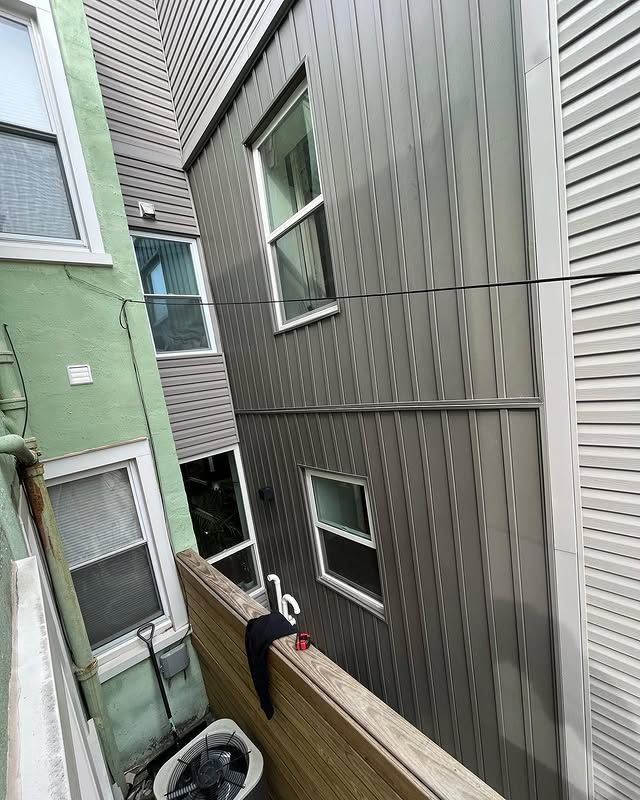 Narrow alley between a green building and a gray building with windows. A wooden fence is in the foreground.
