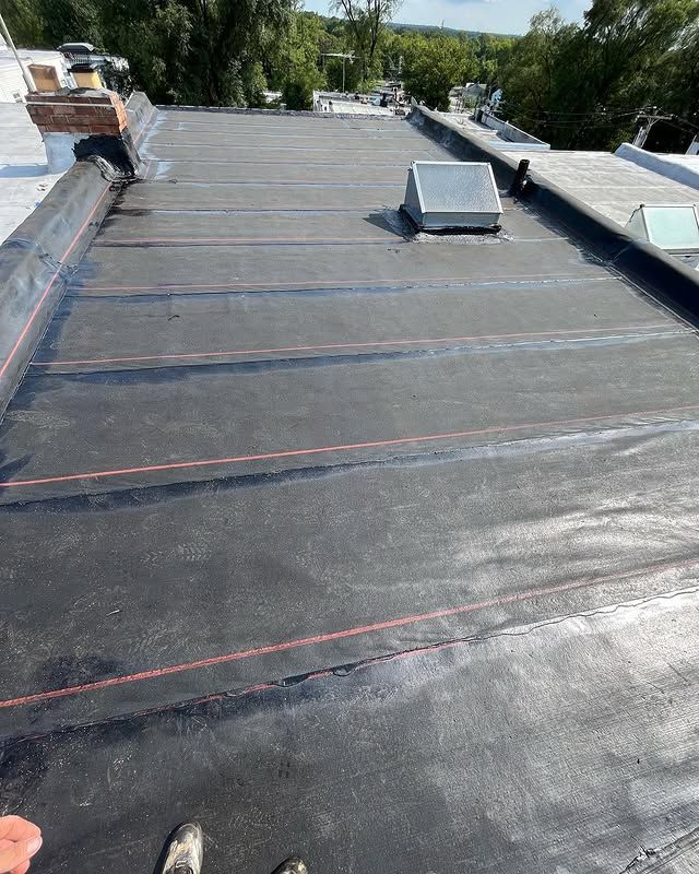 A person is standing on the roof of a building with a black roof.
