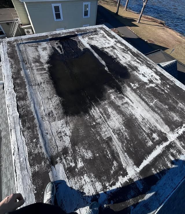 A person is sitting on the roof of a house next to a body of water.