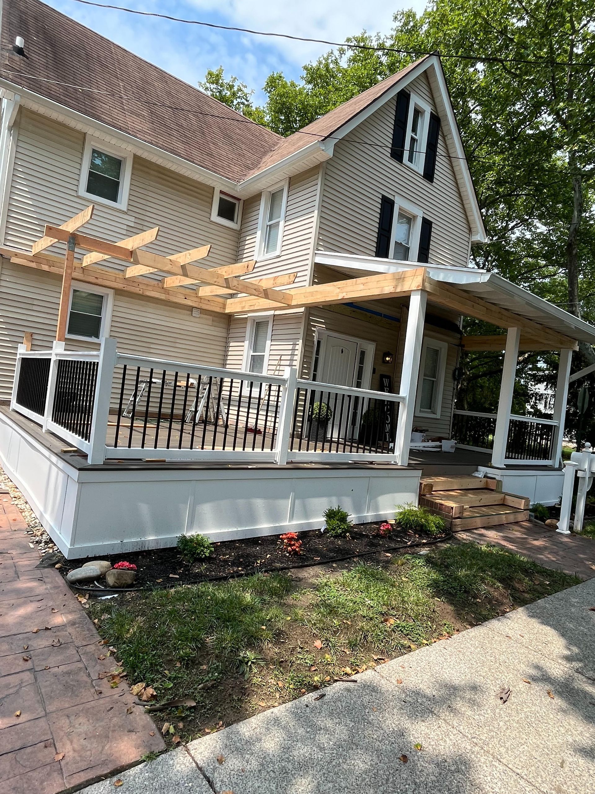 A white house with a large porch and a wooden pergola.