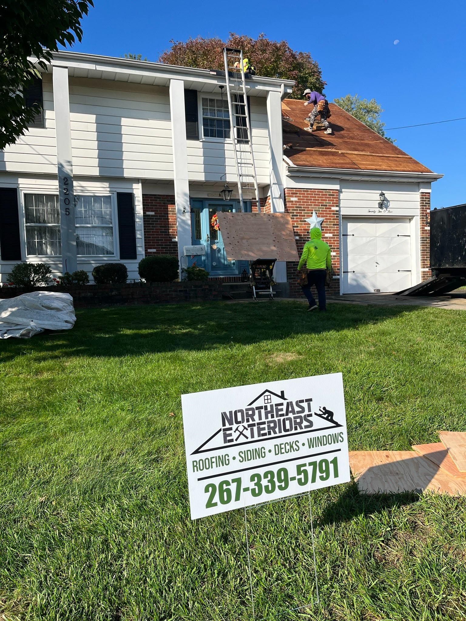 A roofer is working on the roof of a house with a sign in front of it.