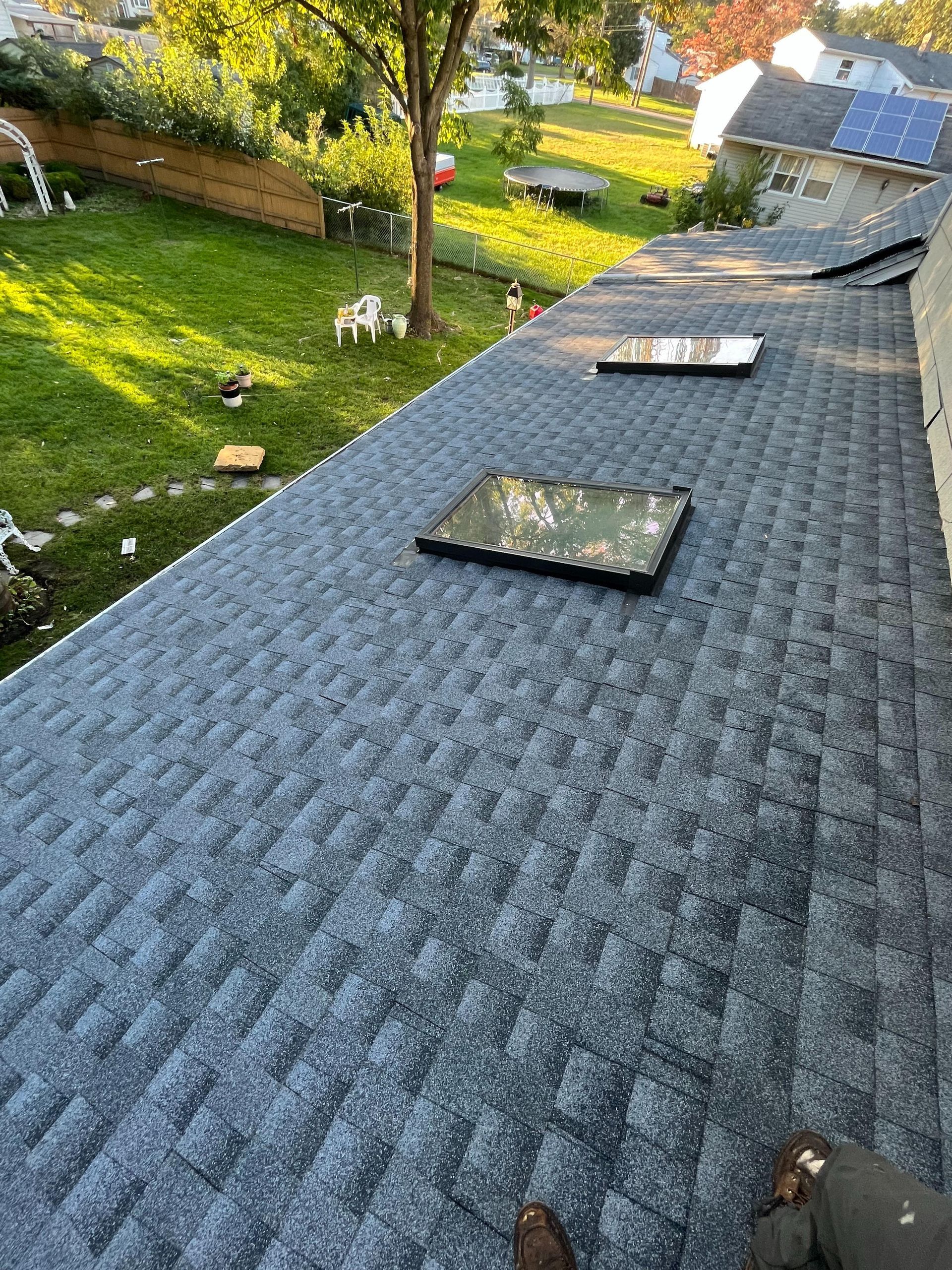 A person is standing on the roof of a house with a skylight.