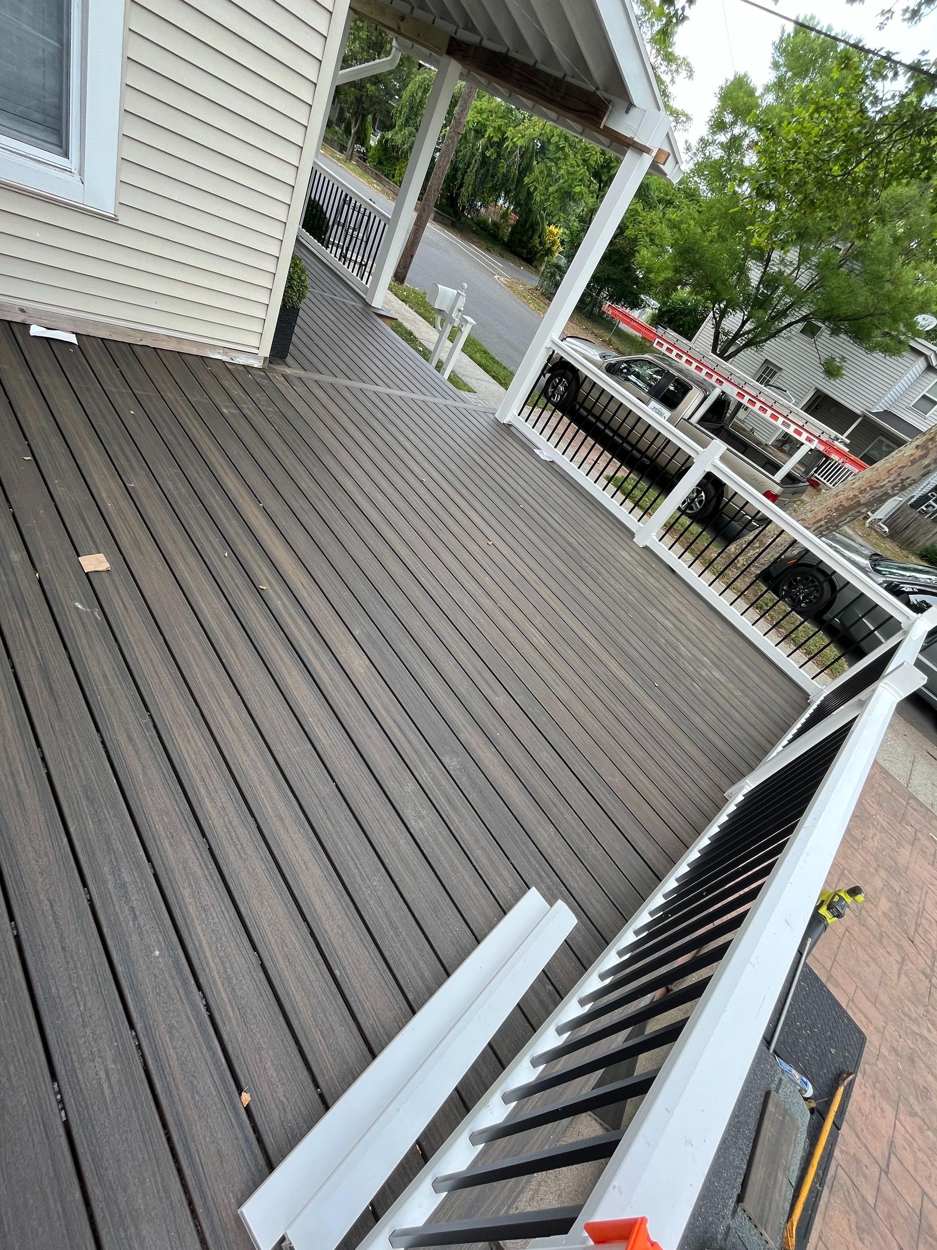 A wooden deck with stairs and a white railing is in front of a house.