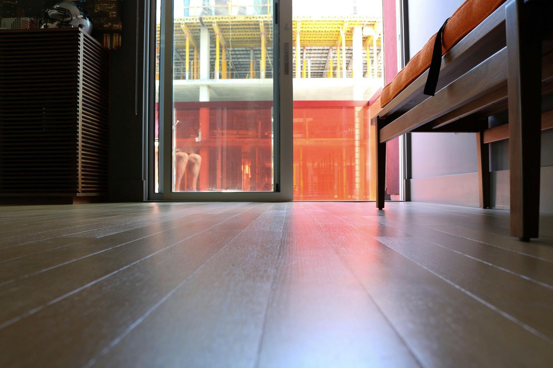 Low-angle view of wood floor with sliding glass door. A bench sits to the right, with a partially visible exterior.
