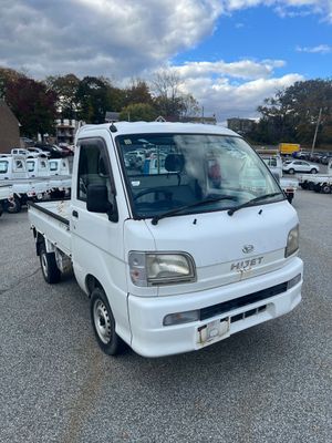 A white Daihatsu Hijet mini truck parked in an outdoor lot on a sunny day.