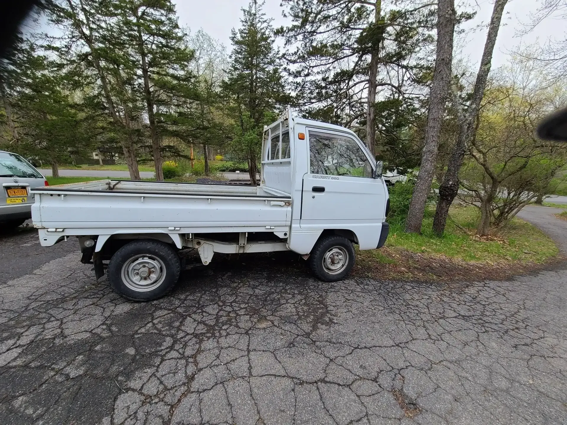 A white Japanese-style kei truck parked on a gravel lot beside trees.