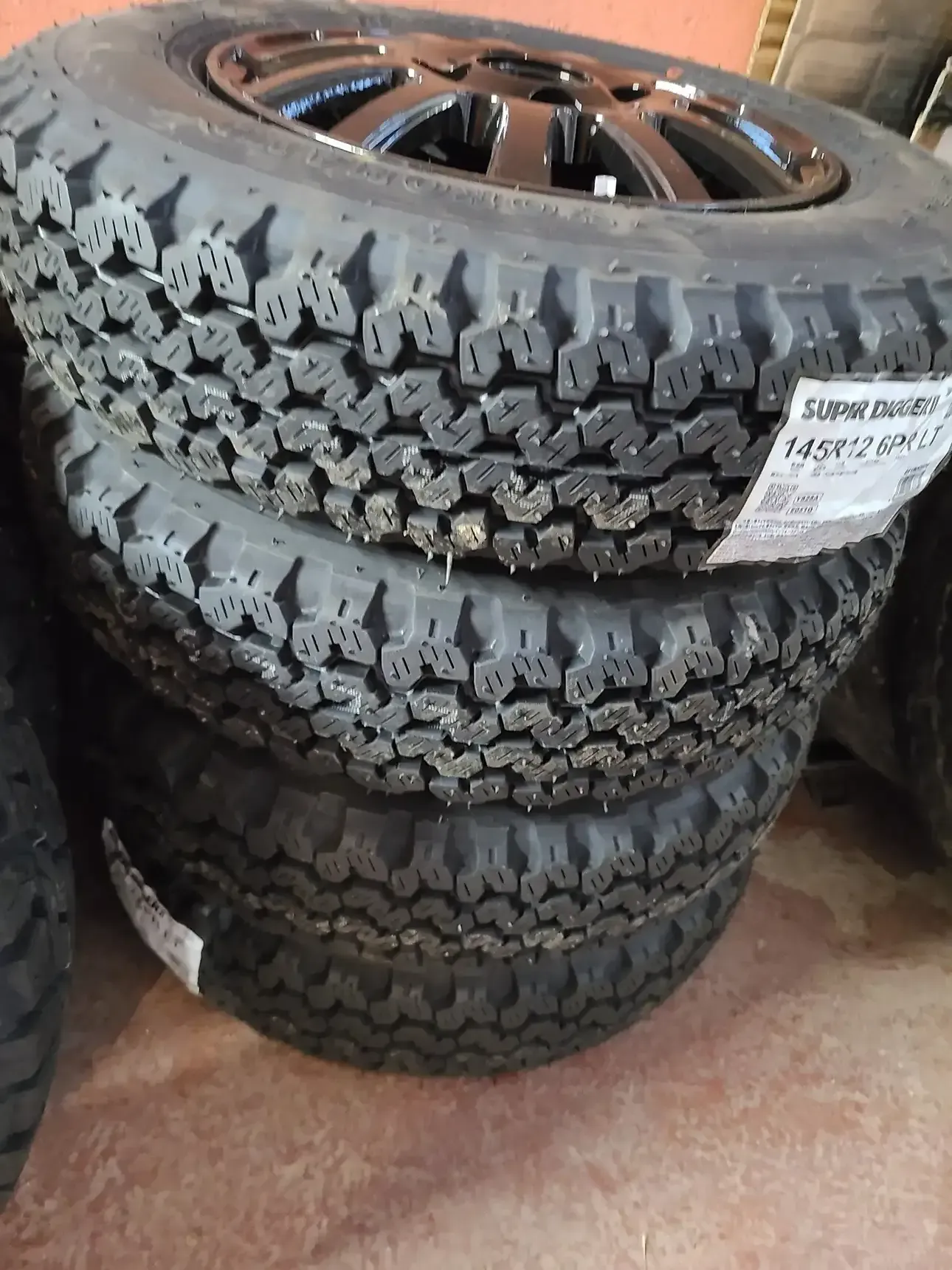 A stack of three black tires with prominent treads, with a wheel rim visible on the top tire.