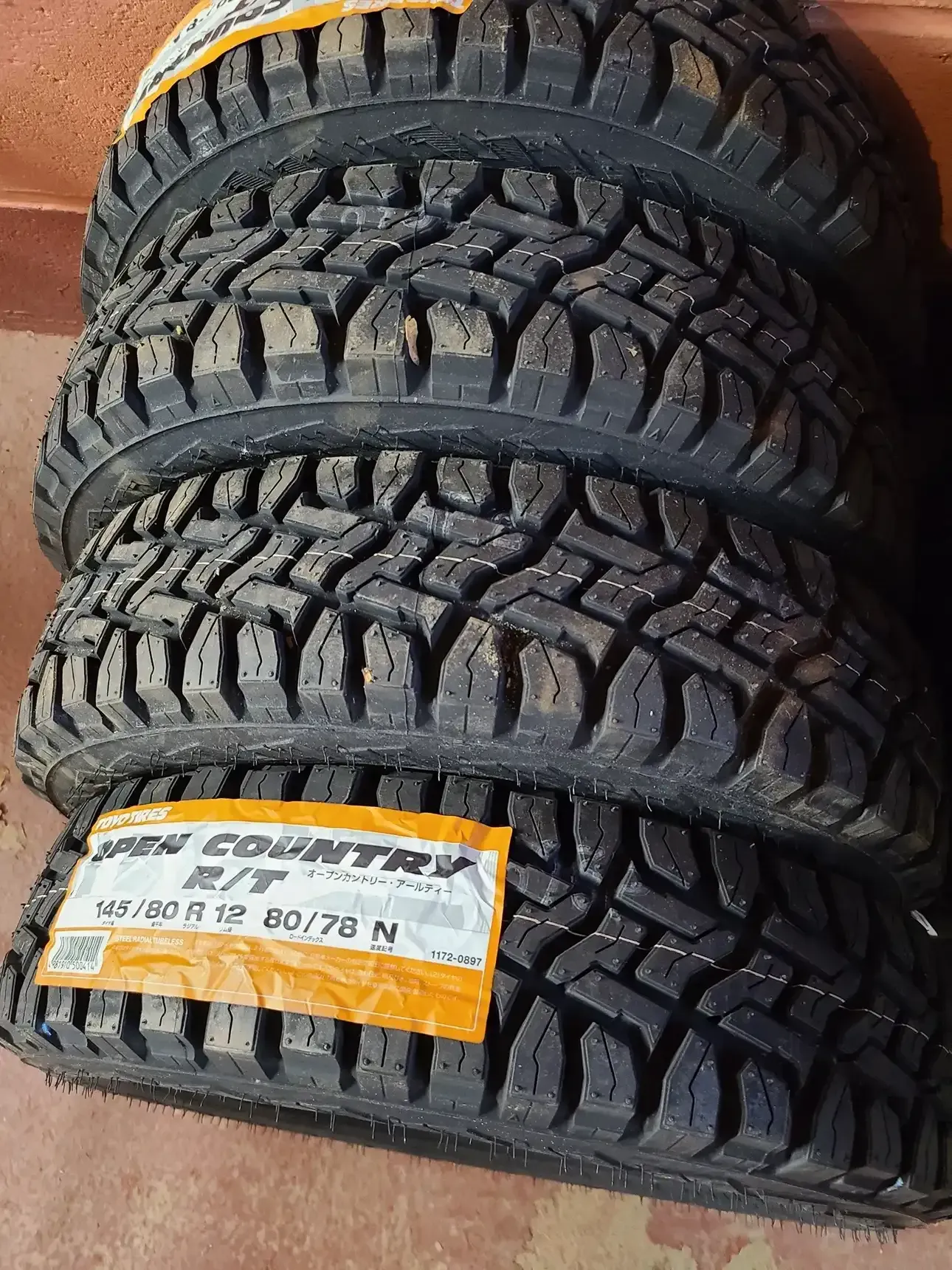 A stack of four new black Toyo Open Country R/T tires with rugged tread patterns, one marked with a label.