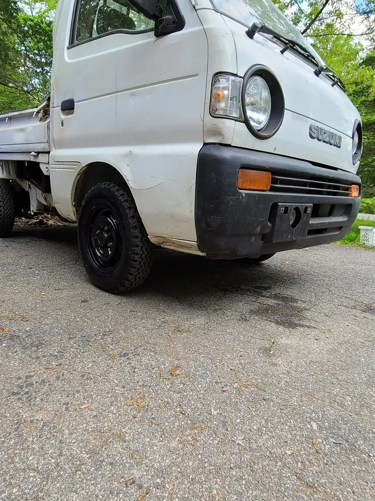 A white Suzuki kei truck parked on a gravel driveway, shown from a low front-quarter angle.
