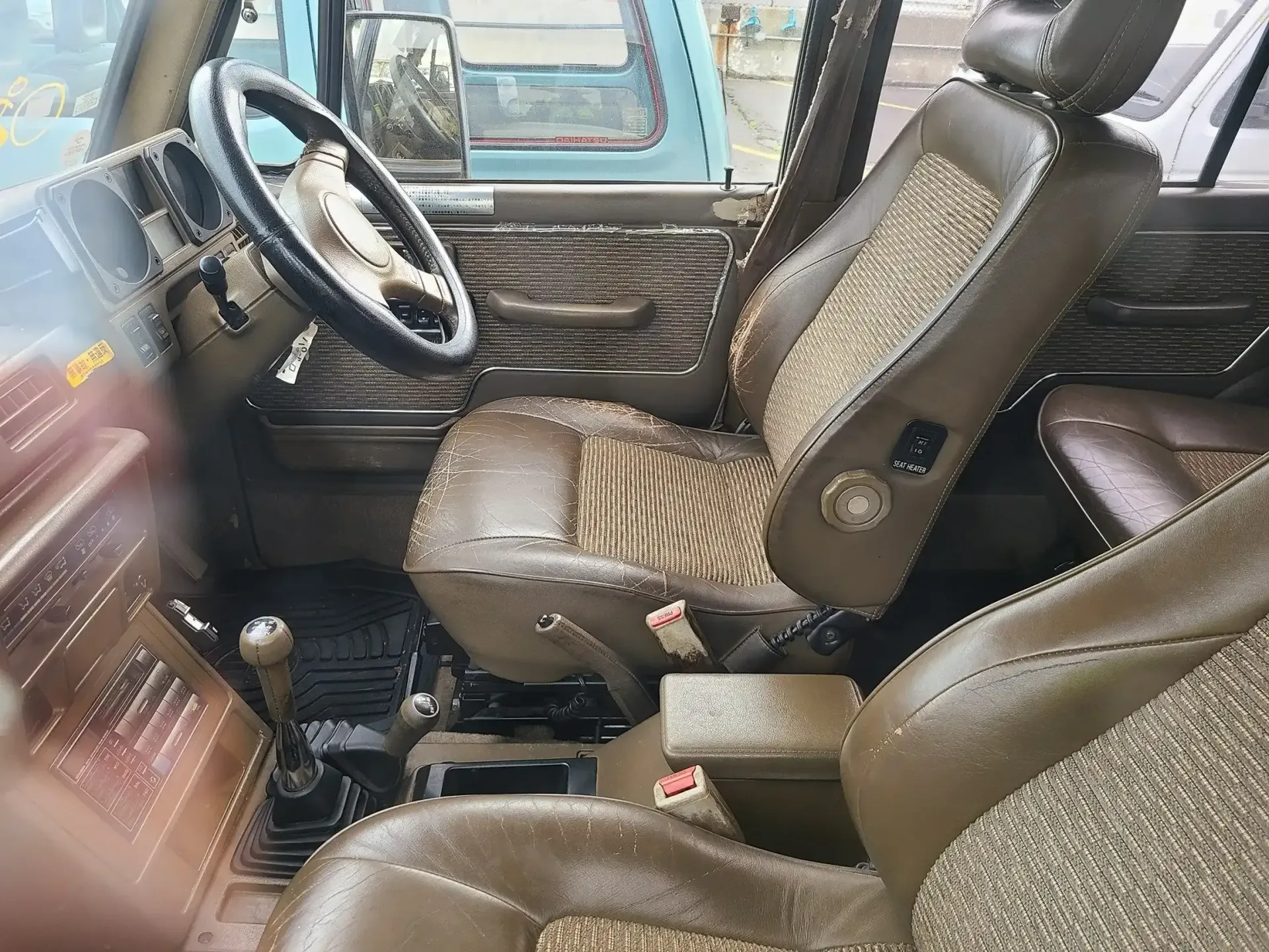 Interior of a vehicle featuring worn, brown leather bucket seats with patterned inserts and a black steering wheel.