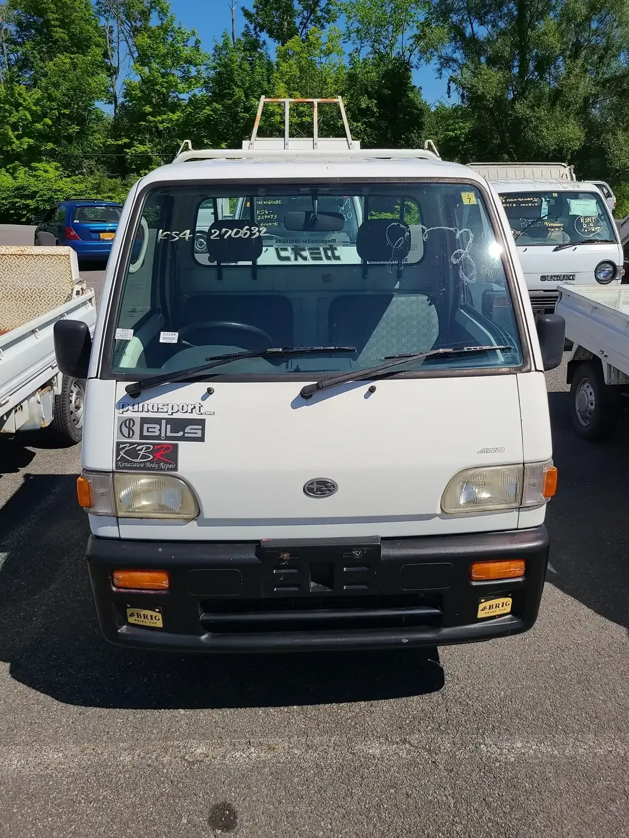 A white, compact Japanese-style cab-over truck parked in a sunny outdoor lot, facing the camera.