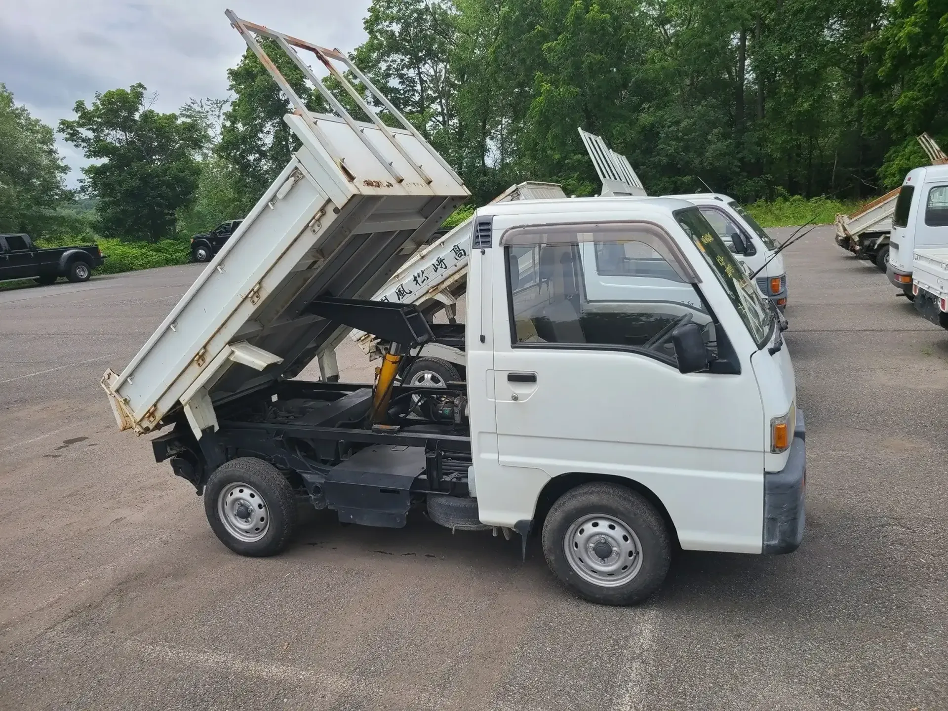 A white mini dump truck parked on a gravel lot with its cargo bed in the raised, tilted position.