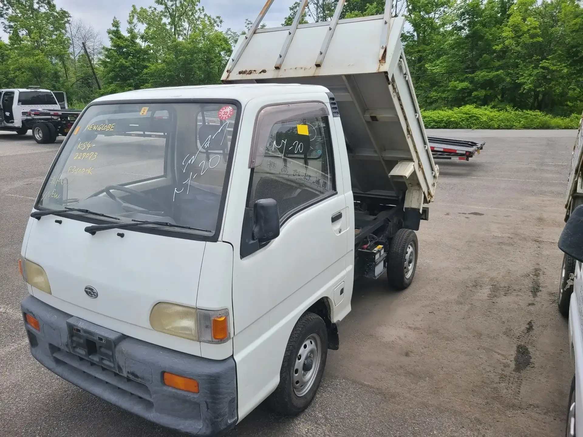 A white kei dump truck parked on a gravel lot with its cargo bed in the raised position.