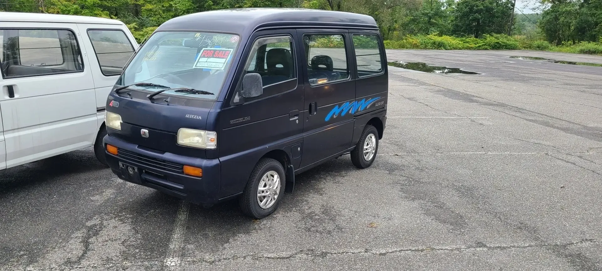 A dark blue minivan parked on a gravel lot next to a white van.