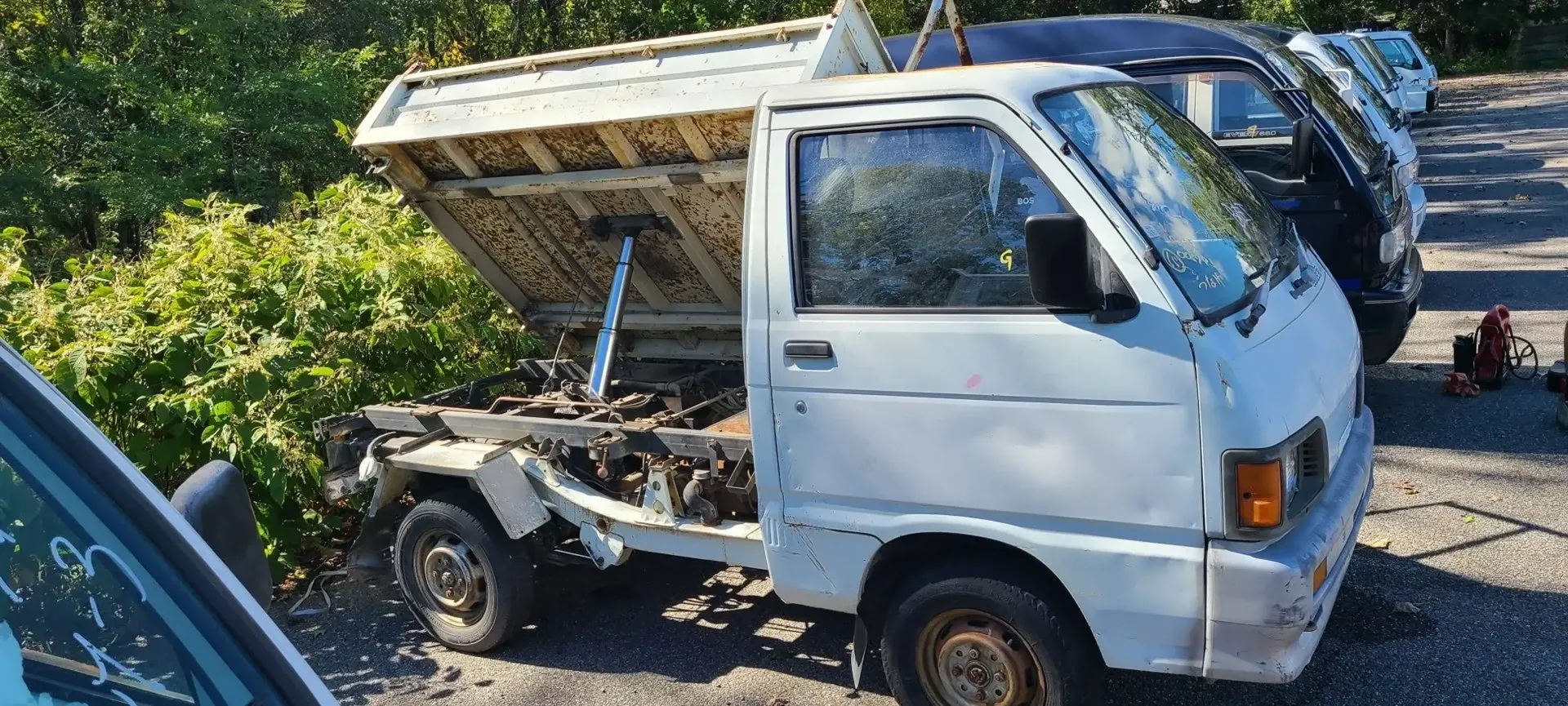 A white kei dump truck sits in a gravel lot with its cargo bed raised.