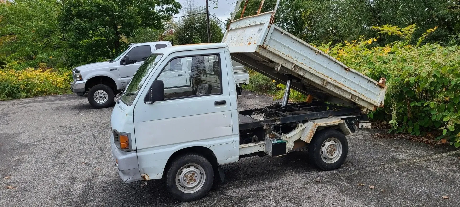 A white kei dump truck parked on a gravel lot with its cargo bed in the raised position.