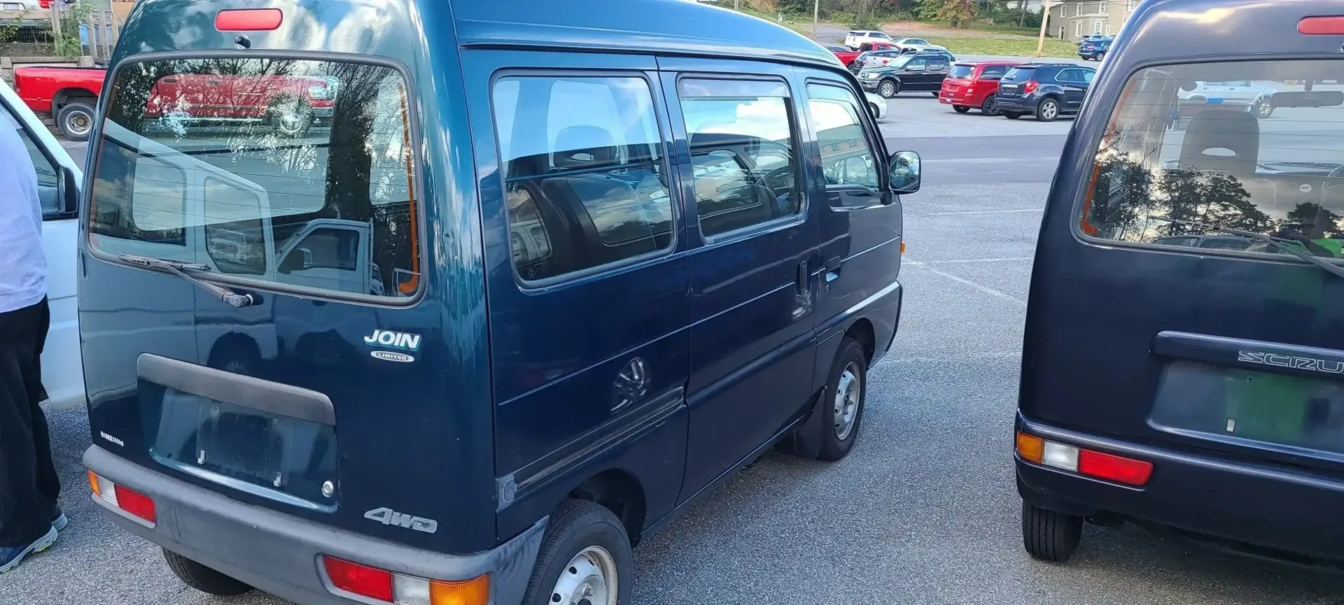 A dark blue minivan parked in a gravel lot next to another vehicle, seen from a high-angle rear perspective.