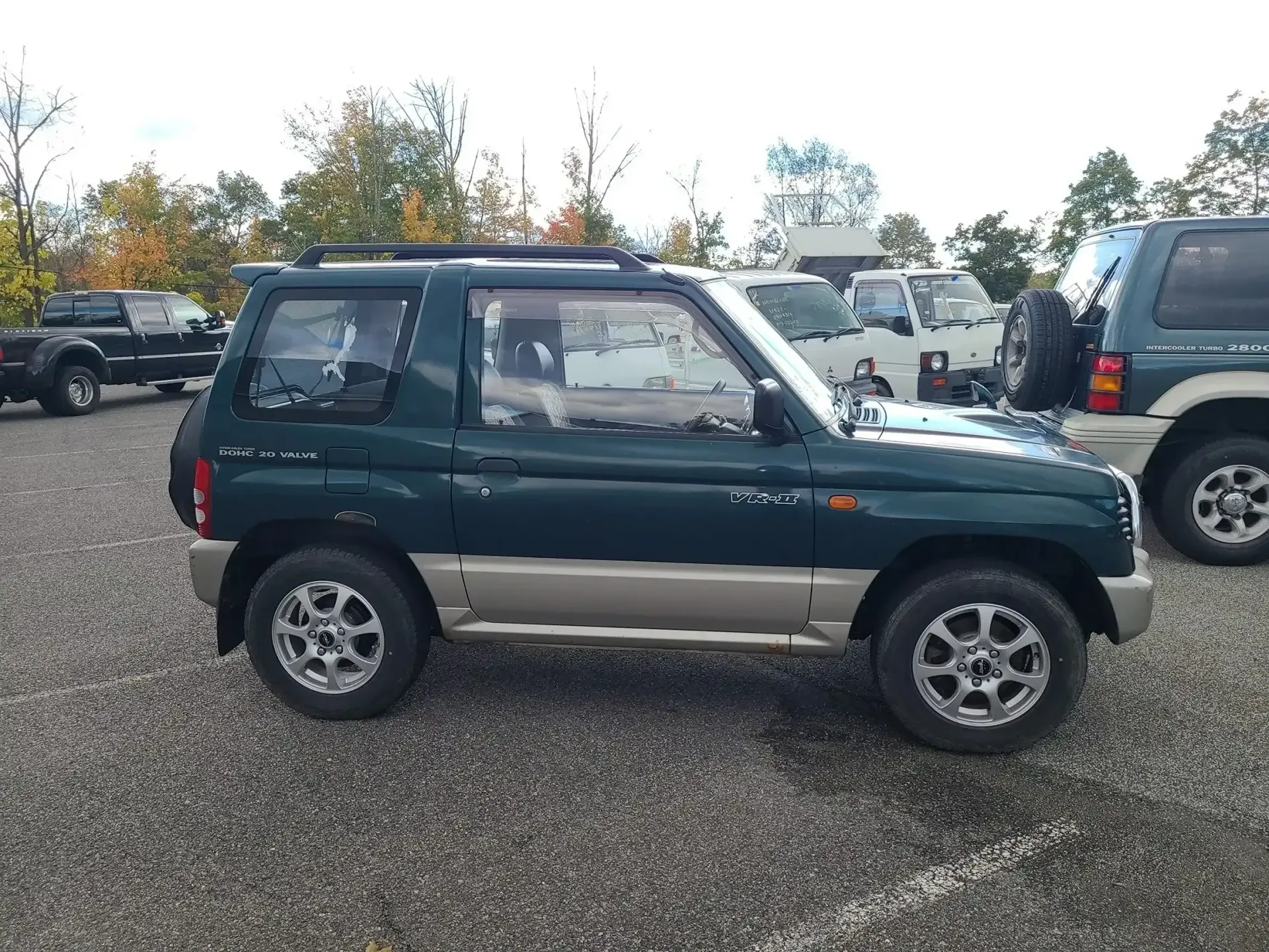 A dark green two-door SUV with tan lower trim parked on a gravel lot, viewed from the side.