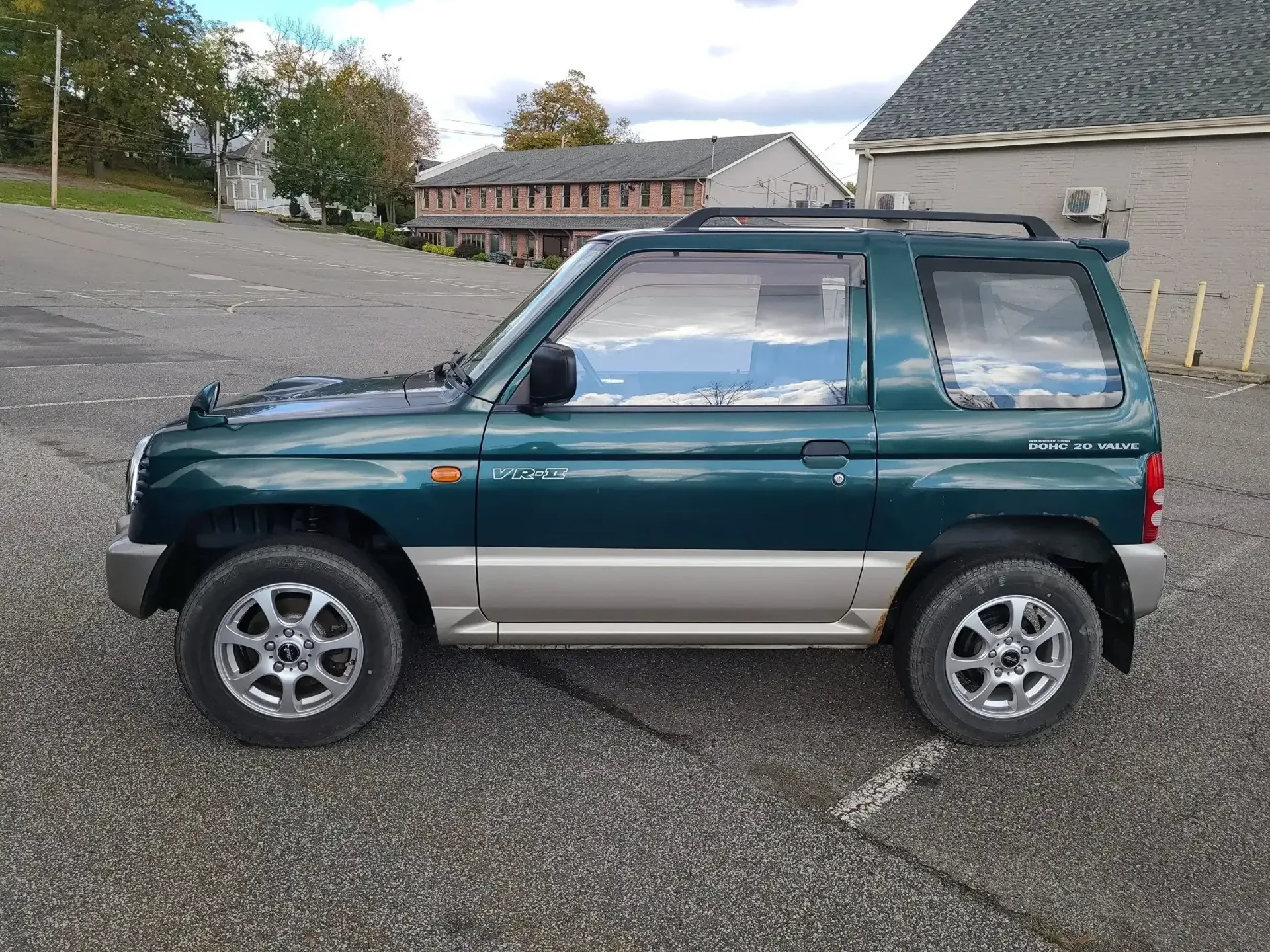 A dark green, two-door Mitsubishi Pajero iO SUV parked on a paved lot with a building in the background.