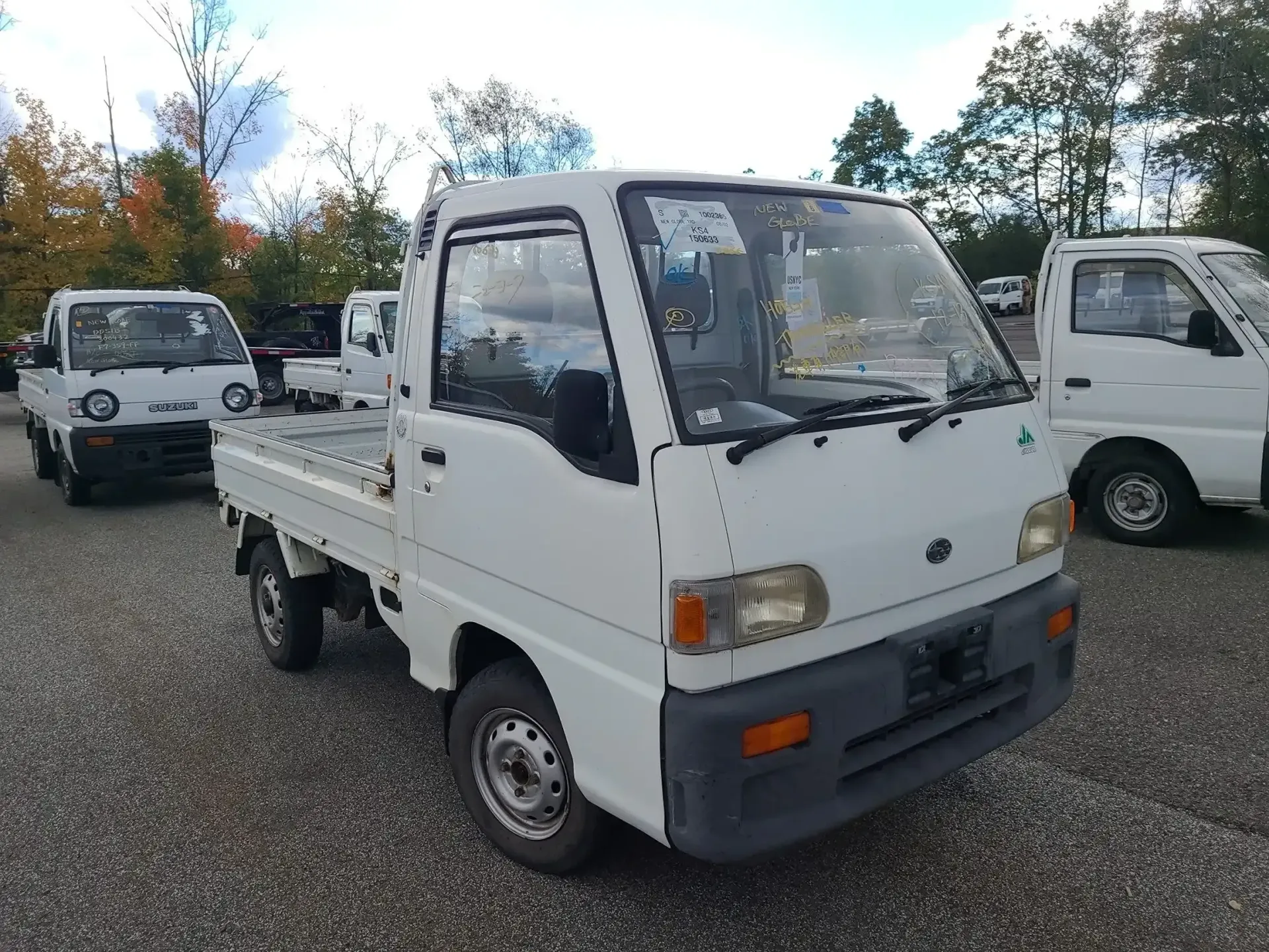 A white kei truck parked on a gravel lot, viewed from a high-angle front three-quarter perspective.