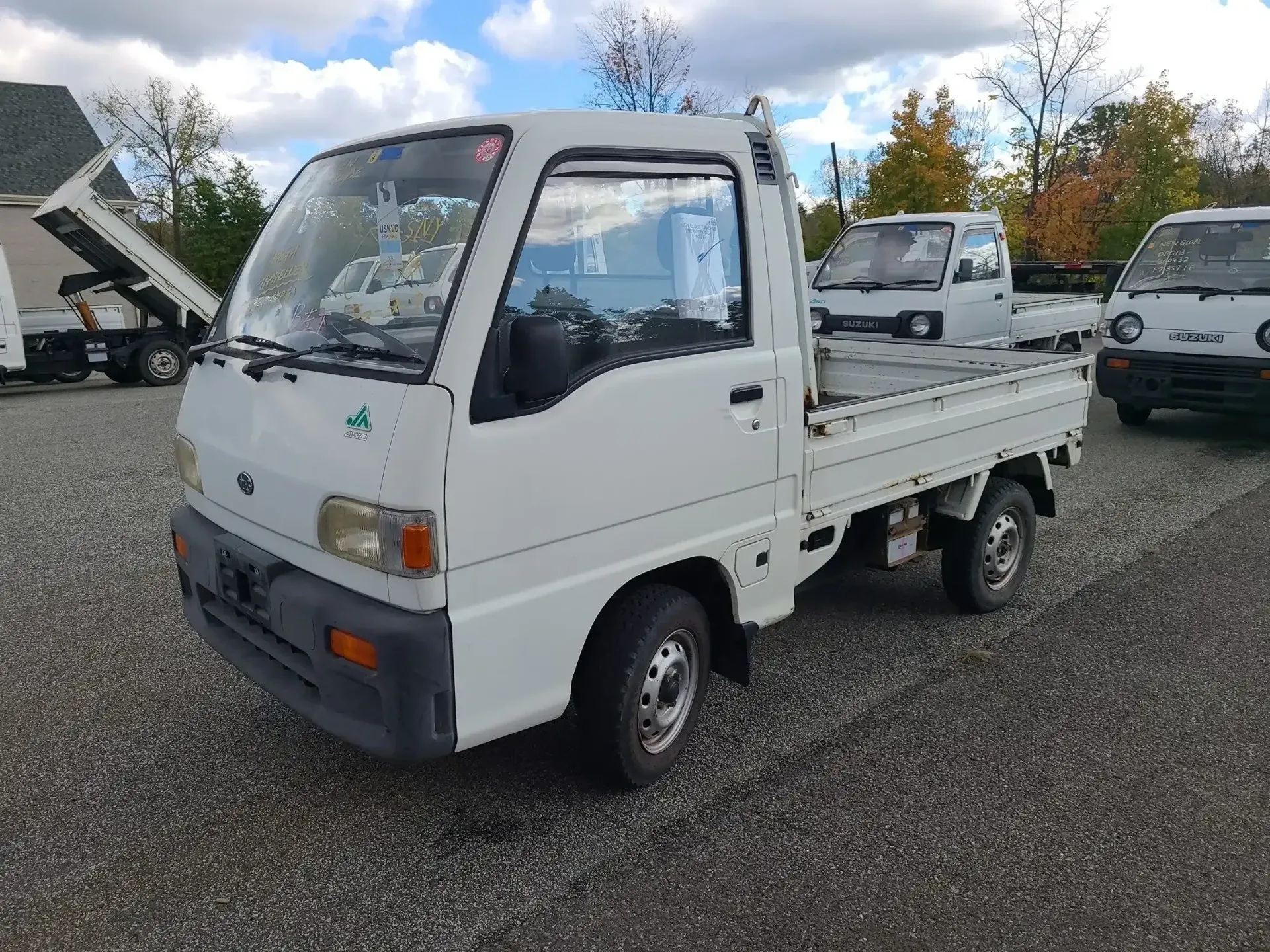 A white compact pickup truck parked on a gravel lot with other similar small vehicles in the background.