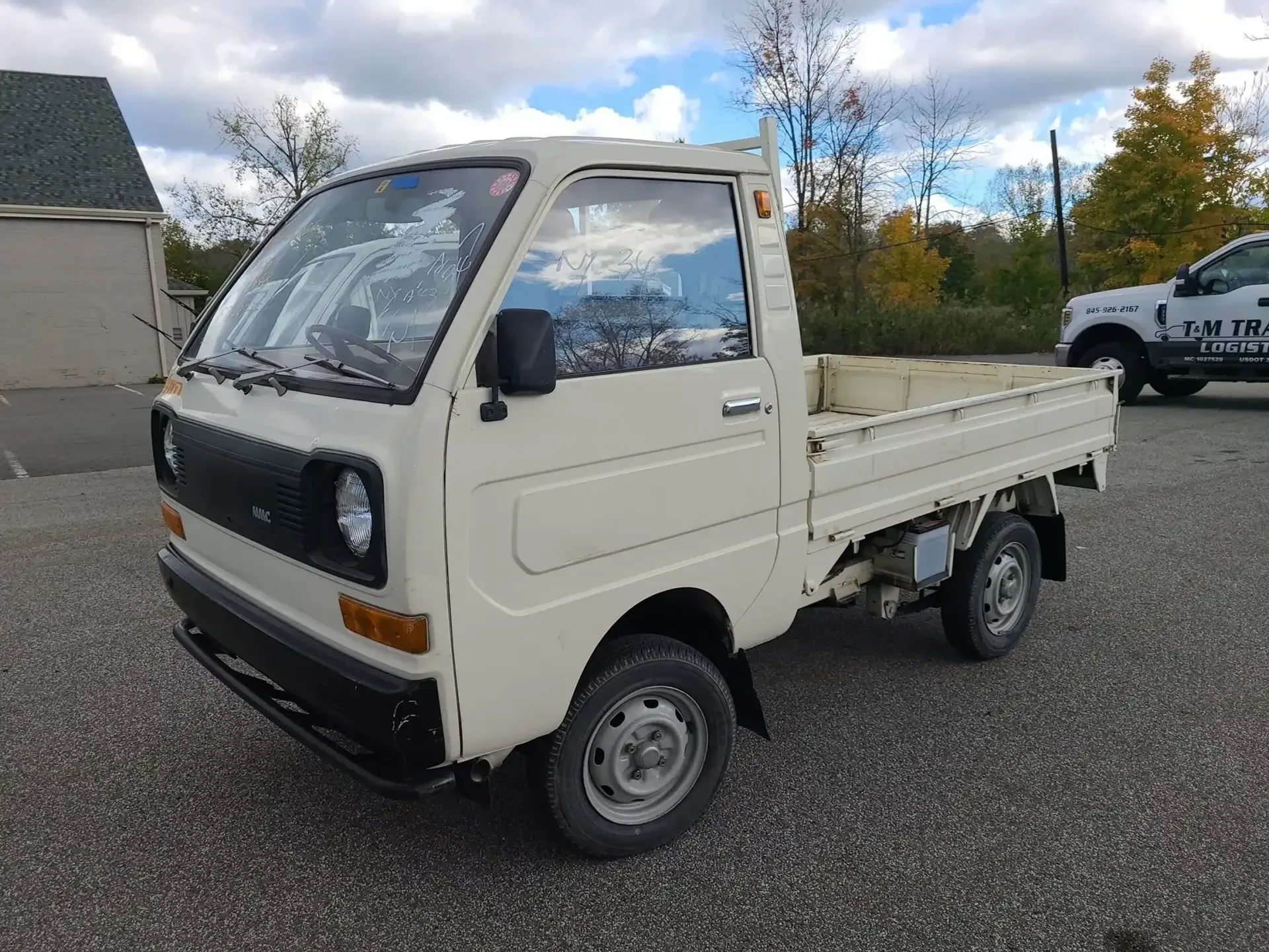 A white kei truck parked on a gravel lot under a cloudy sky.