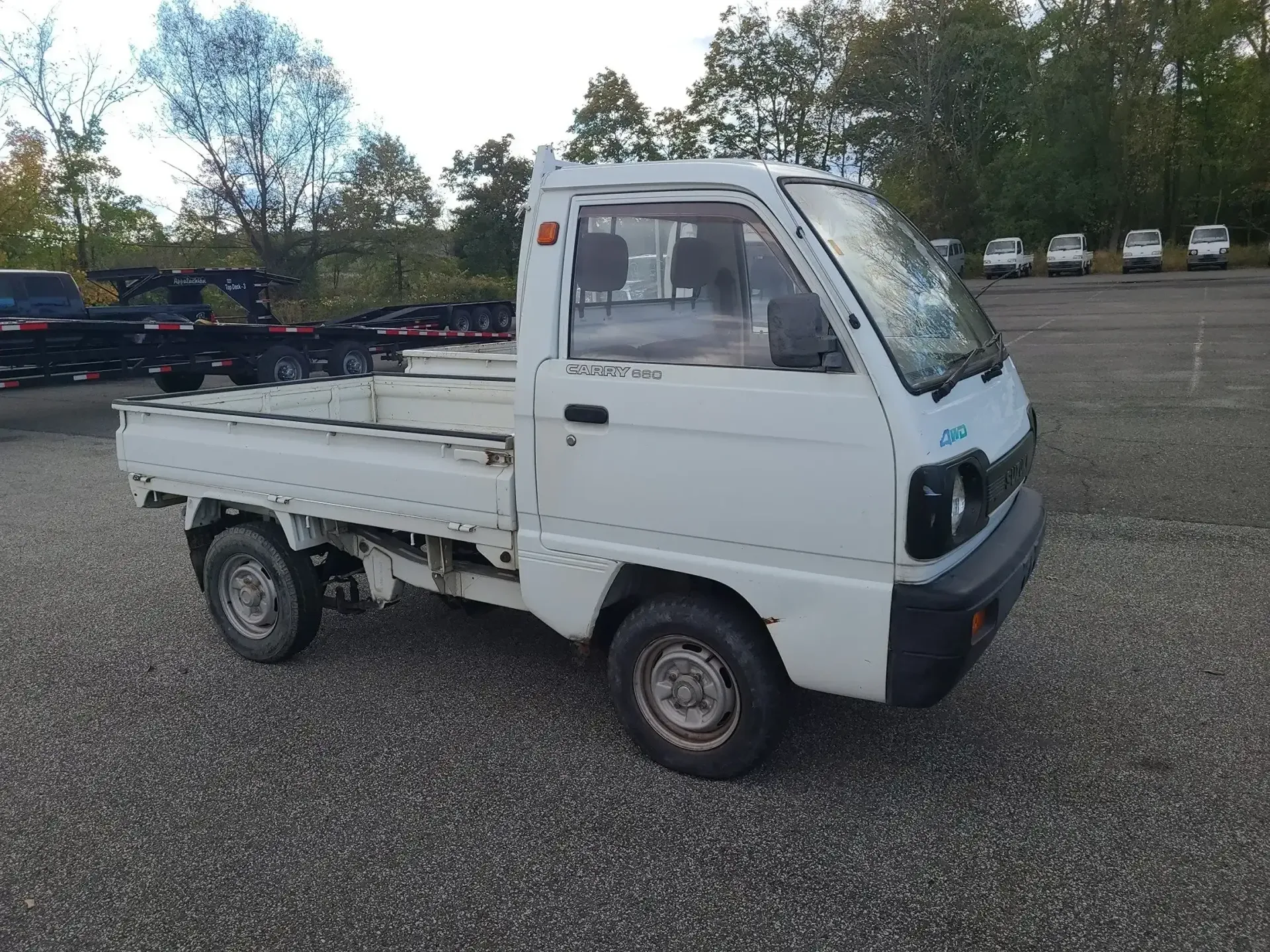 A white, compact kei truck parked on a gravel lot with trees in the background.