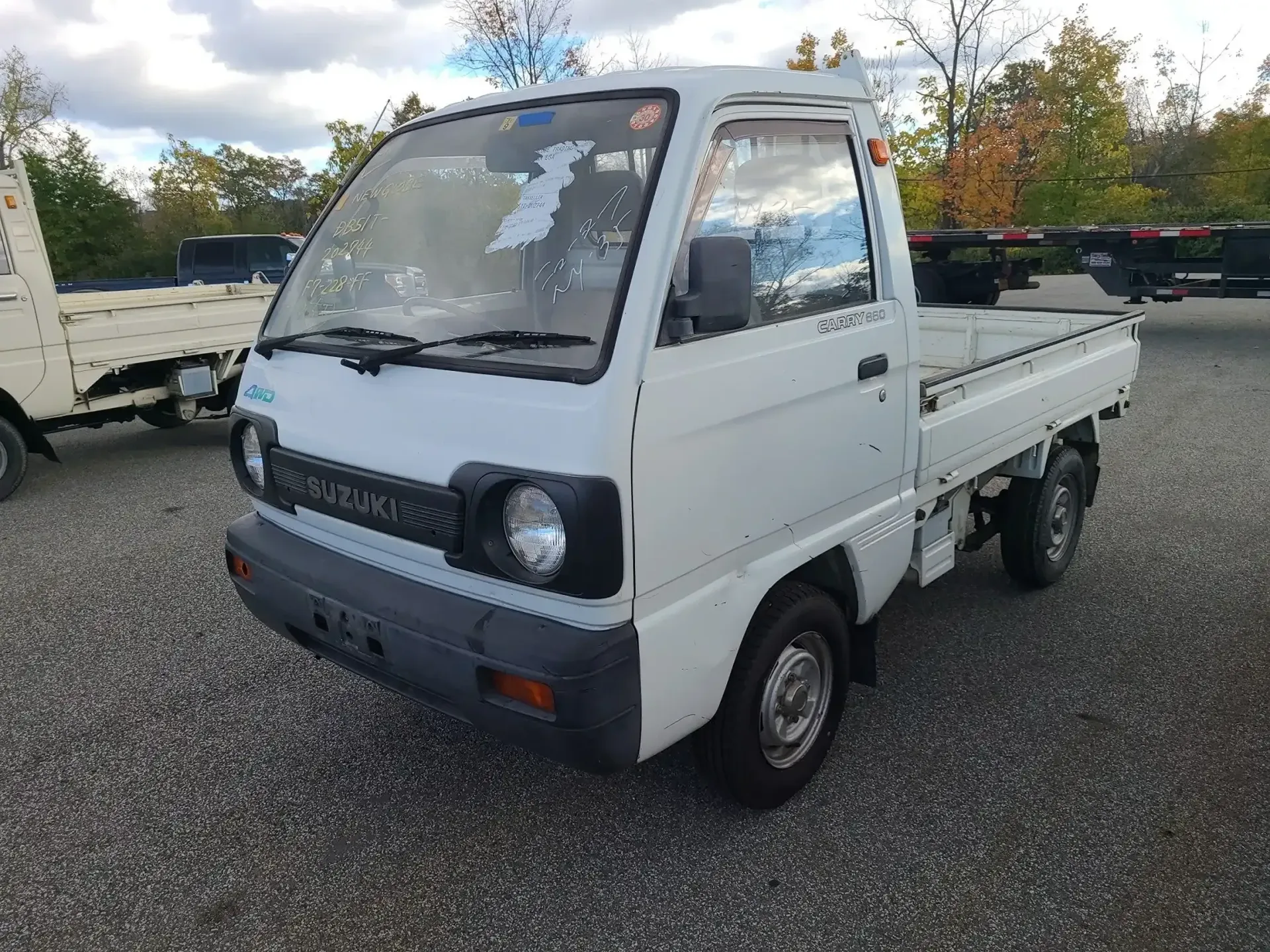 A white mini truck parked on a gravel lot under a cloudy sky.