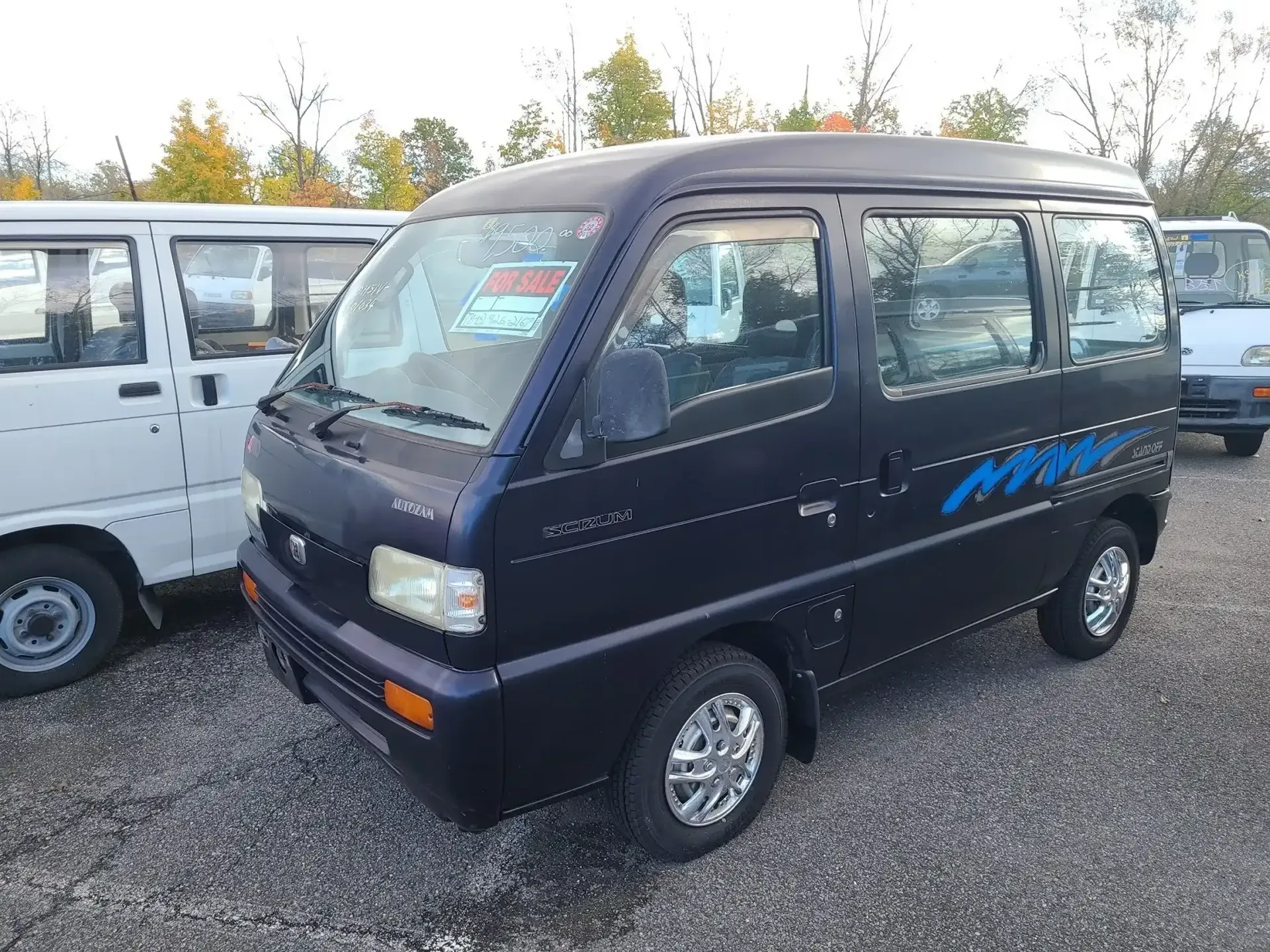 A dark blue minivan parked on a gravel lot next to a white van.