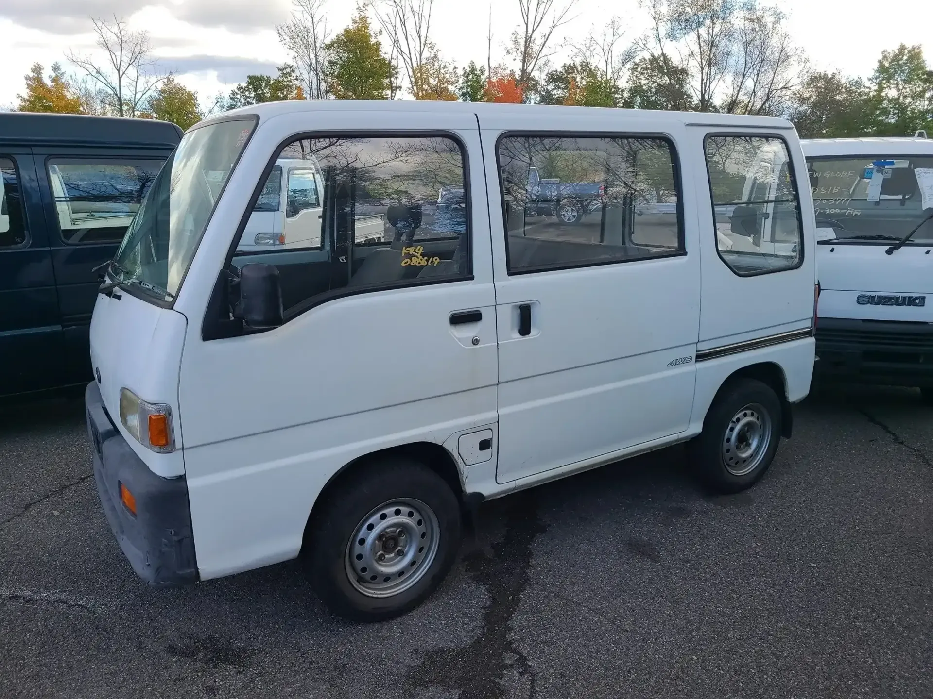 A small, white, boxy Japanese kei van parked outdoors on an asphalt lot.