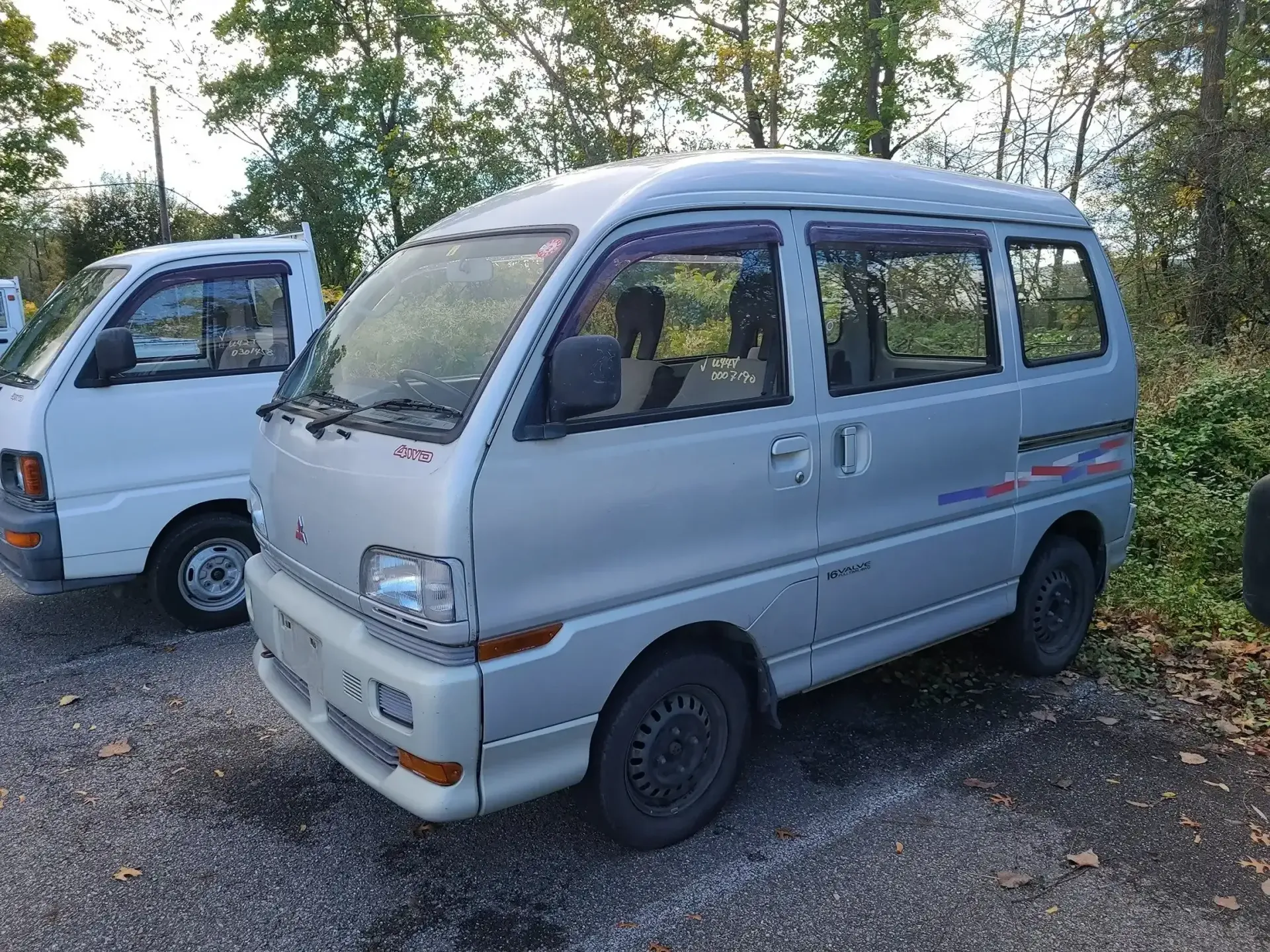 A silver minivan parked on a gravel lot next to a white pickup truck on a sunny day.